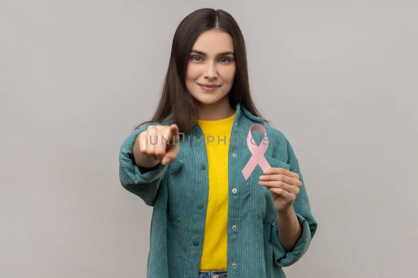 Woman holding pink ribbon, symbol of breast cancer awareness, looking and pointing at camera. by Khosro1