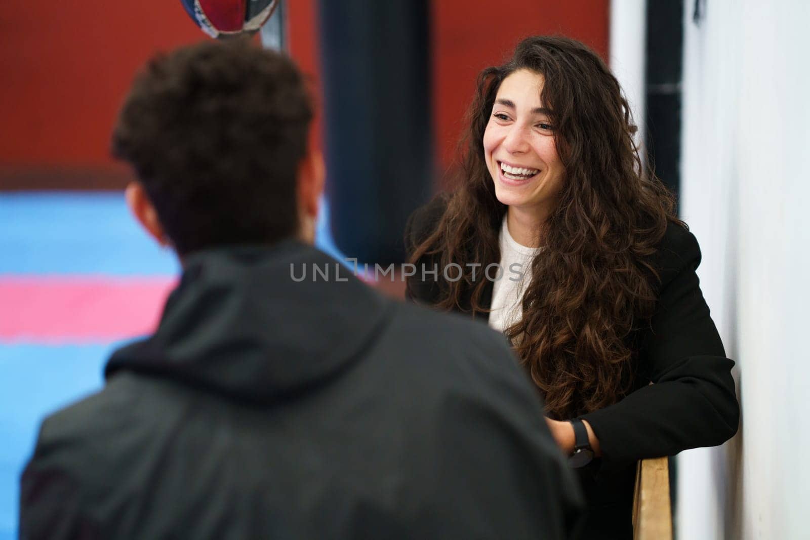 Happy young woman talking with sportsman and laughing while sitting on bench during psychology session in gym