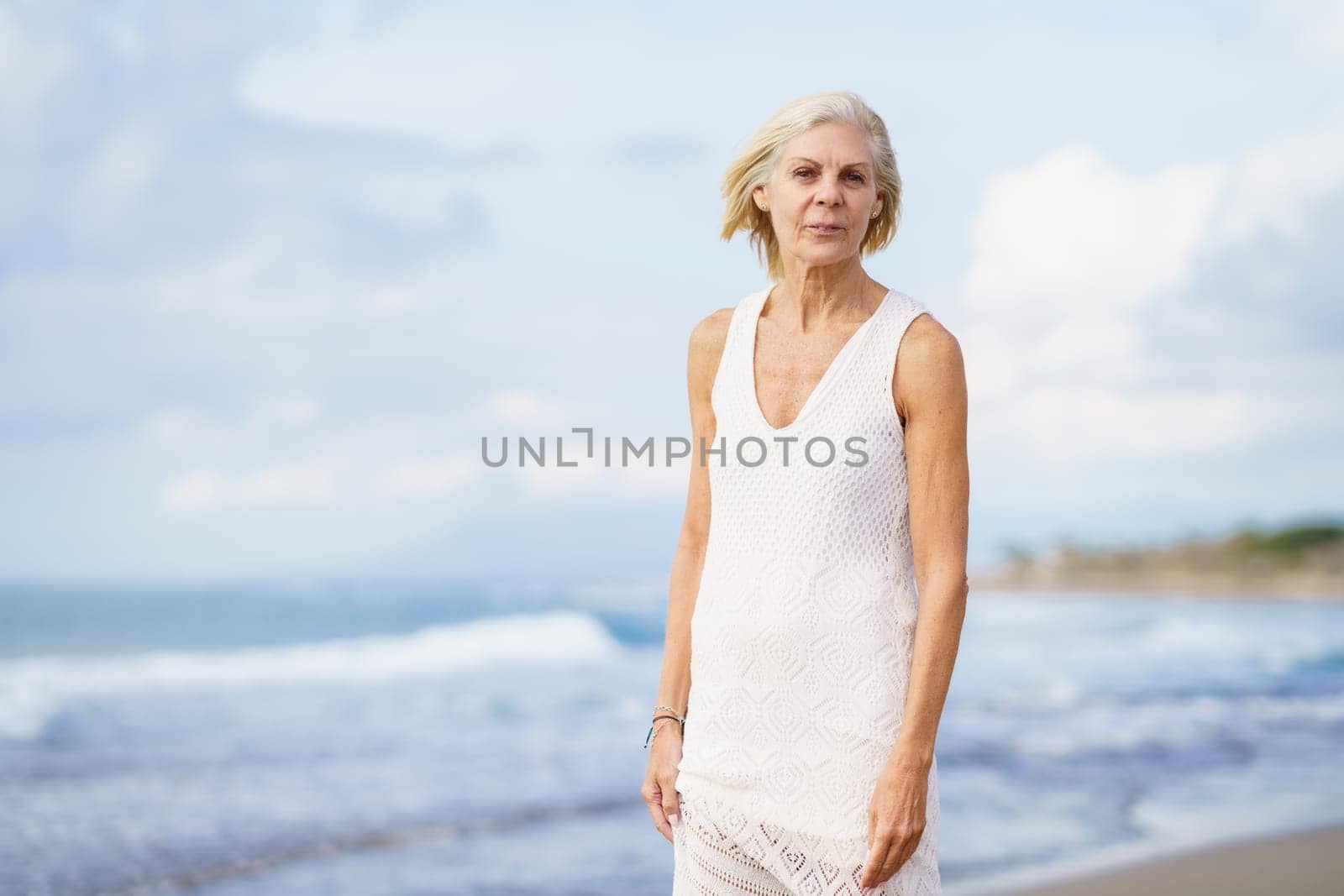 Portrait of smiling mature woman walking on the beach. Elderly female enjoying her retirement at a seaside location.