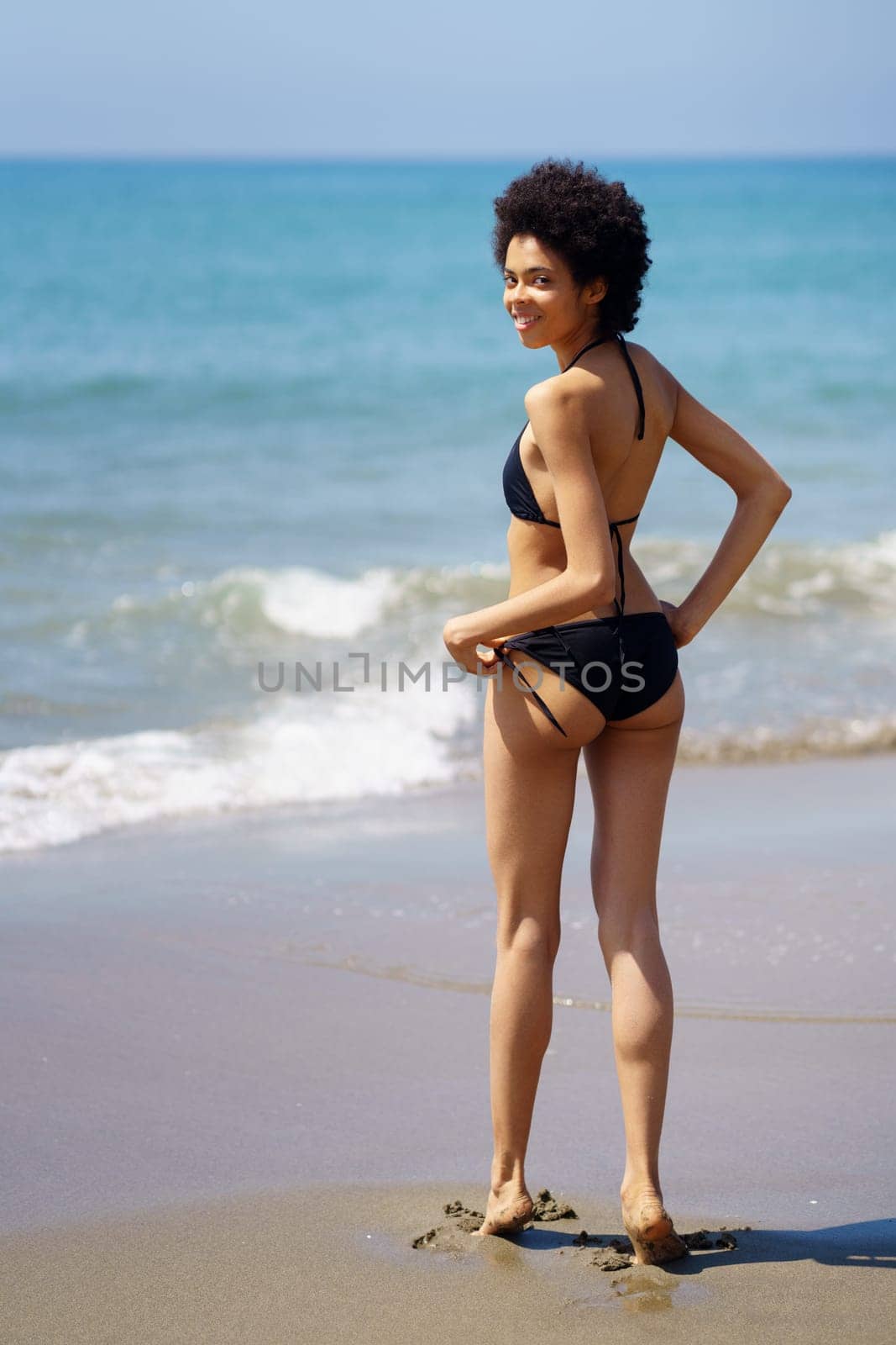 Optimistic black woman in swimwear on beach by javiindy