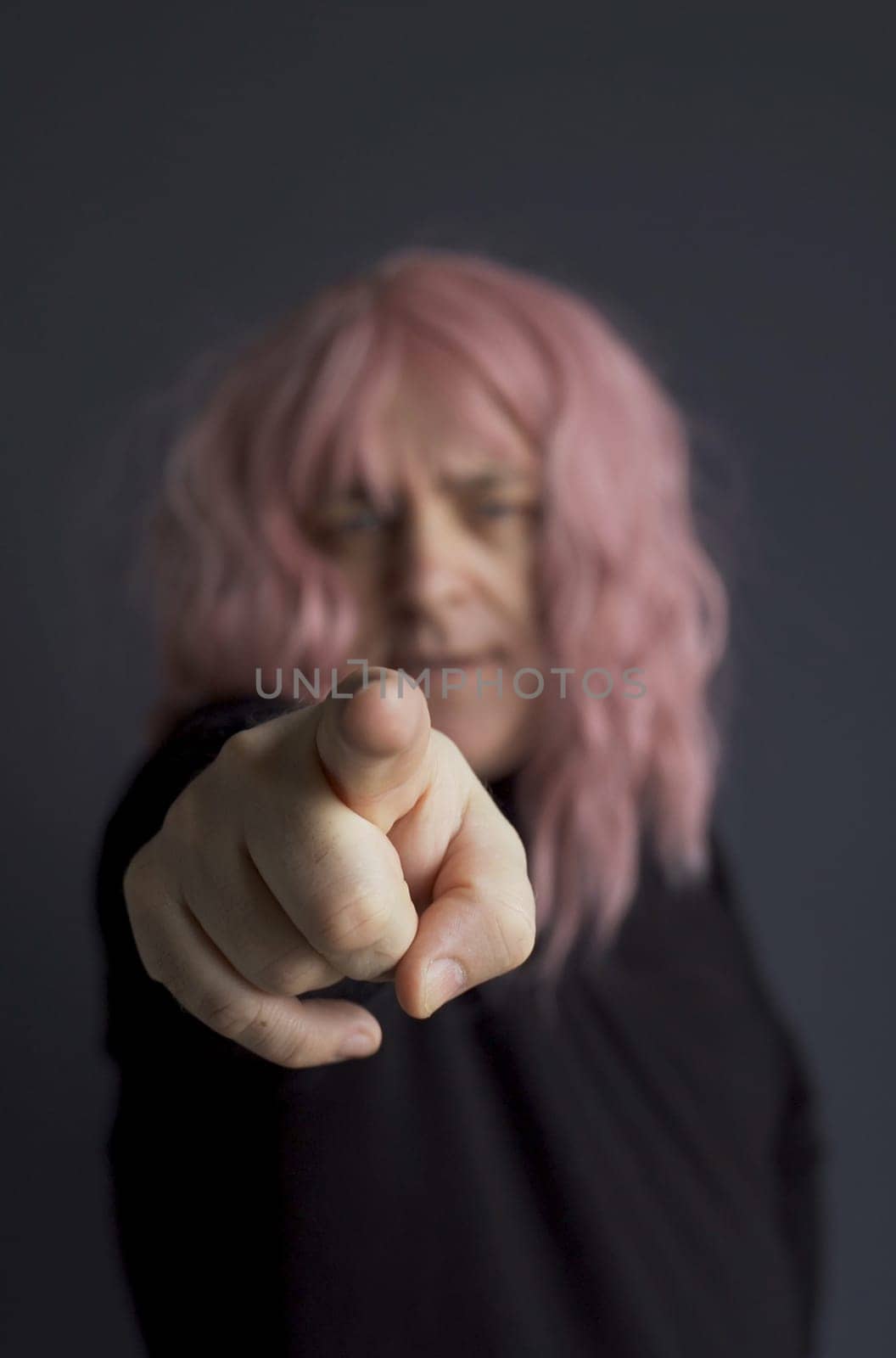 Portrait of a man in a pink wig, looking and pointing his finger at the camera. close-up. Vertical frame.