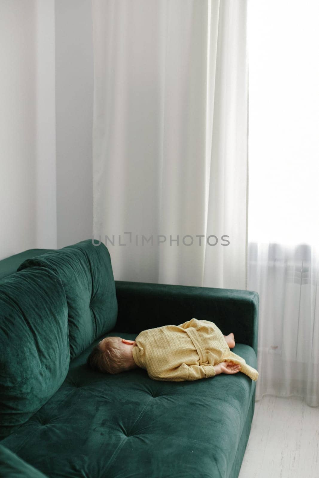 A little tired boy in a bathrobe fell asleep on the sofa.