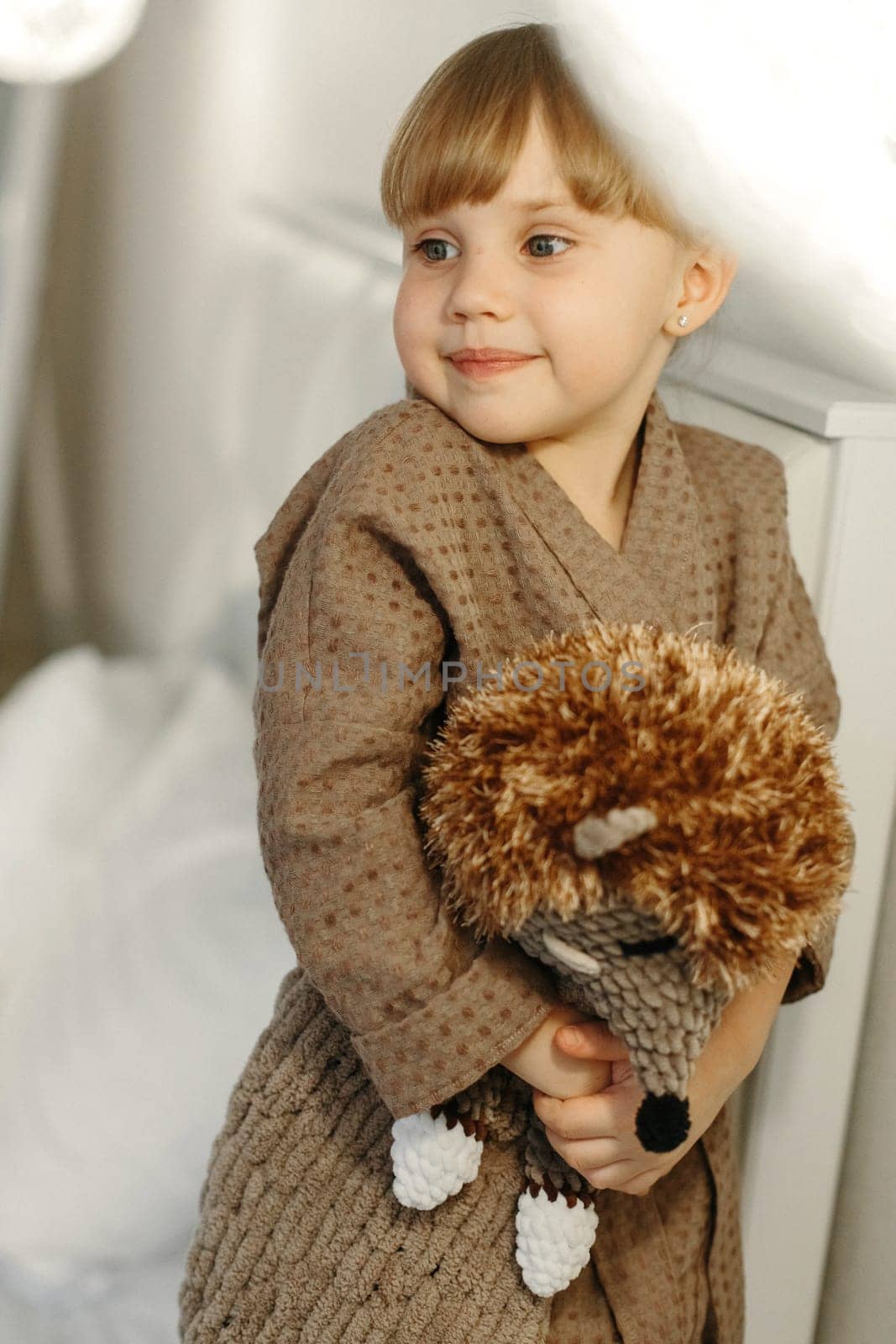 A girl in a dressing gown plays with a knitted hedgehog in the room.