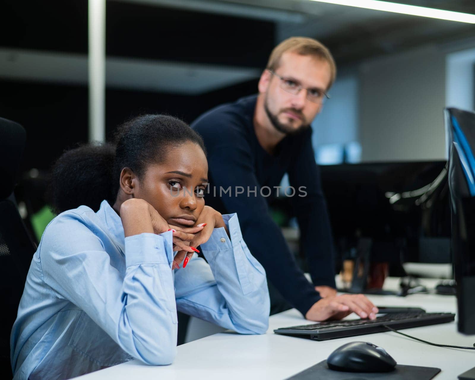 Colleagues look at the monitor and decide working moments. Caucasian man helps sad african woman solve computer problem. by mrwed54