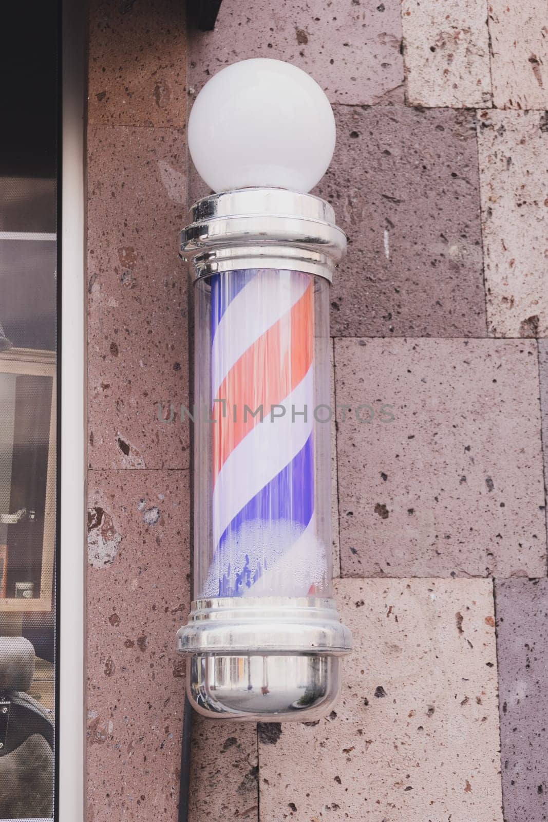 Barber sign and male hairdresser pole or staff mounted on wall. Helix of colored stripes red white and blue.