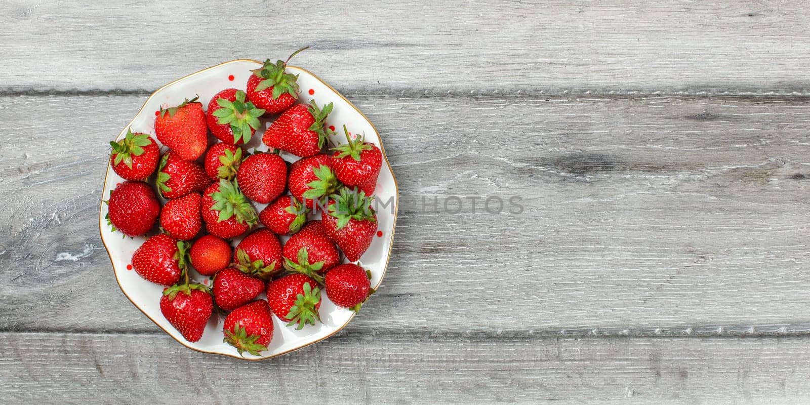 Tabletop view - plate with strawberries on gray wooden desk, place for text on right. by Ivanko