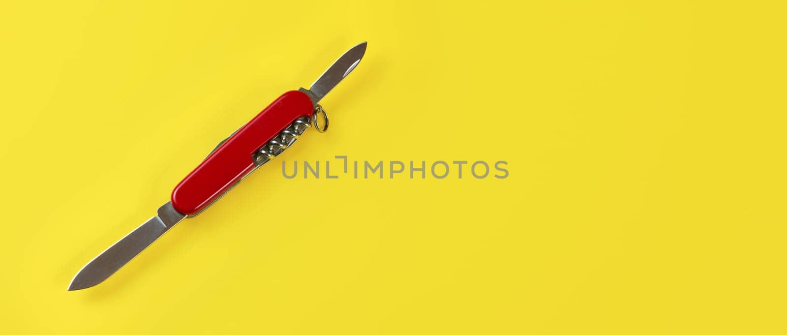 Table top view, red pocket knife with both blades opened, on yellow board. Space for text on right. by Ivanko