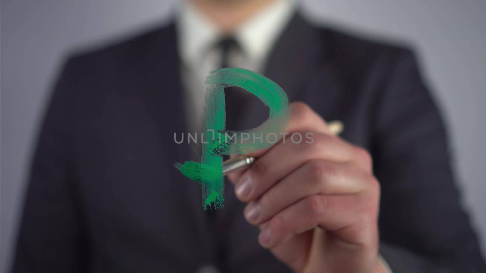 A businessman draws on the glass the currency symbol of the Russian ruble. A man in a suit draws on glass with a brush and green paint. 4k