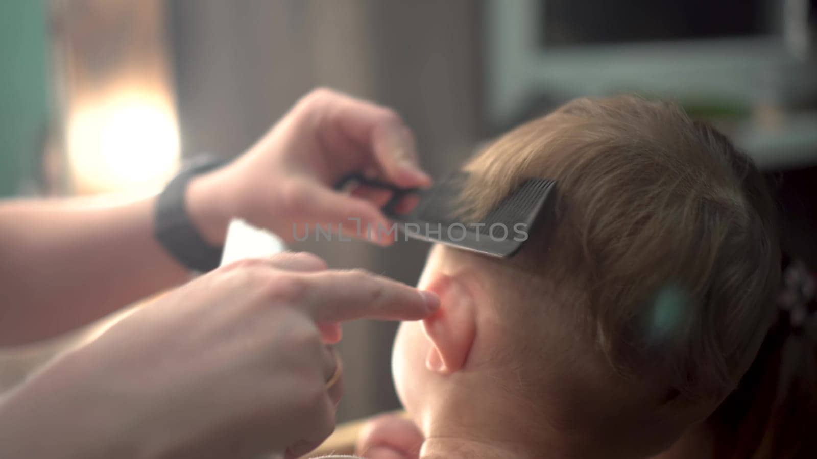 A small child is having a haircut. The boy is sitting on a chair and his mother is cutting his hair. Haircut with a barber machine. 4k