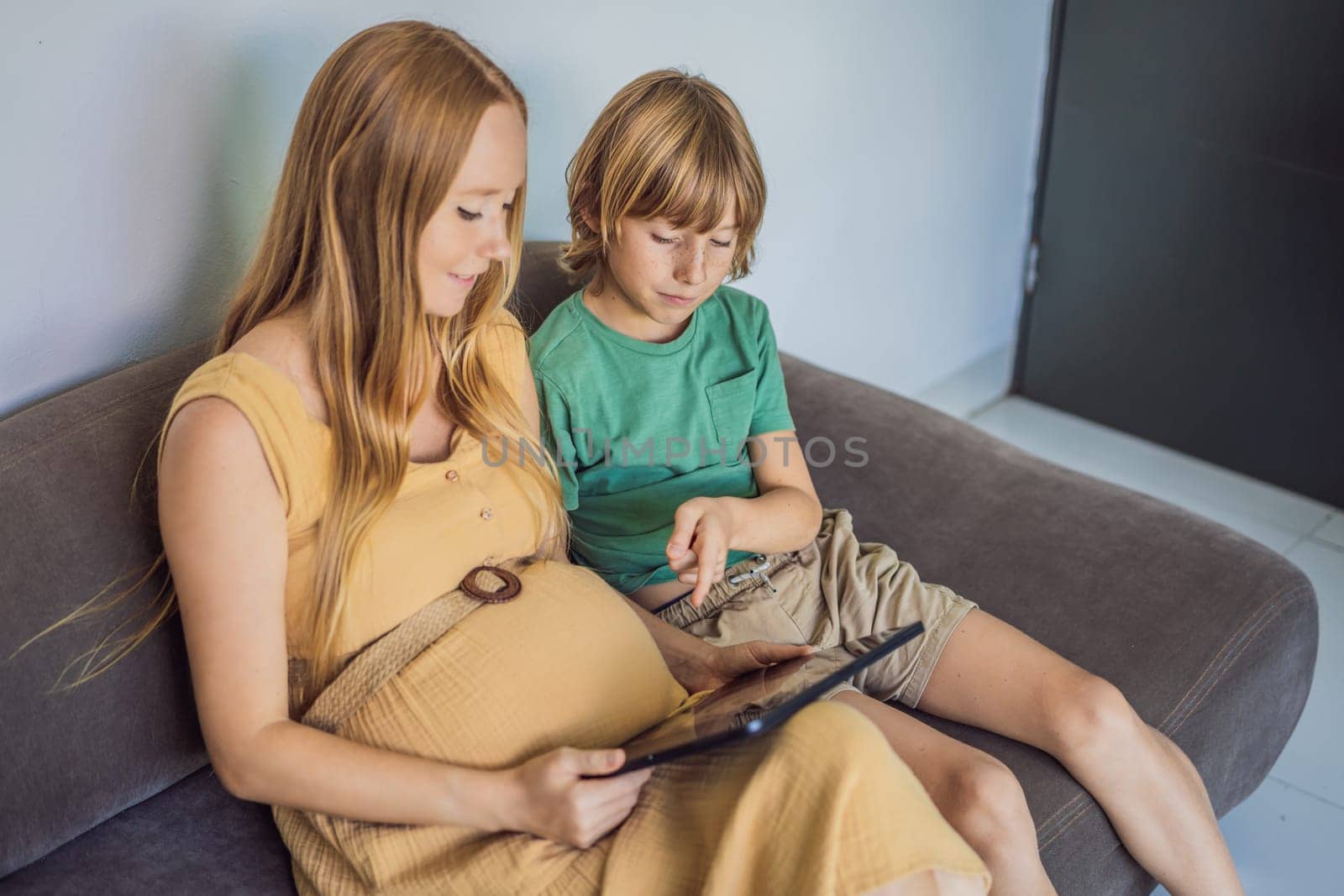 Mom and her son looking on ultrasound image of his unborn baby brother on mothers tablet. Concept of healthcare and family happiness expecting baby.