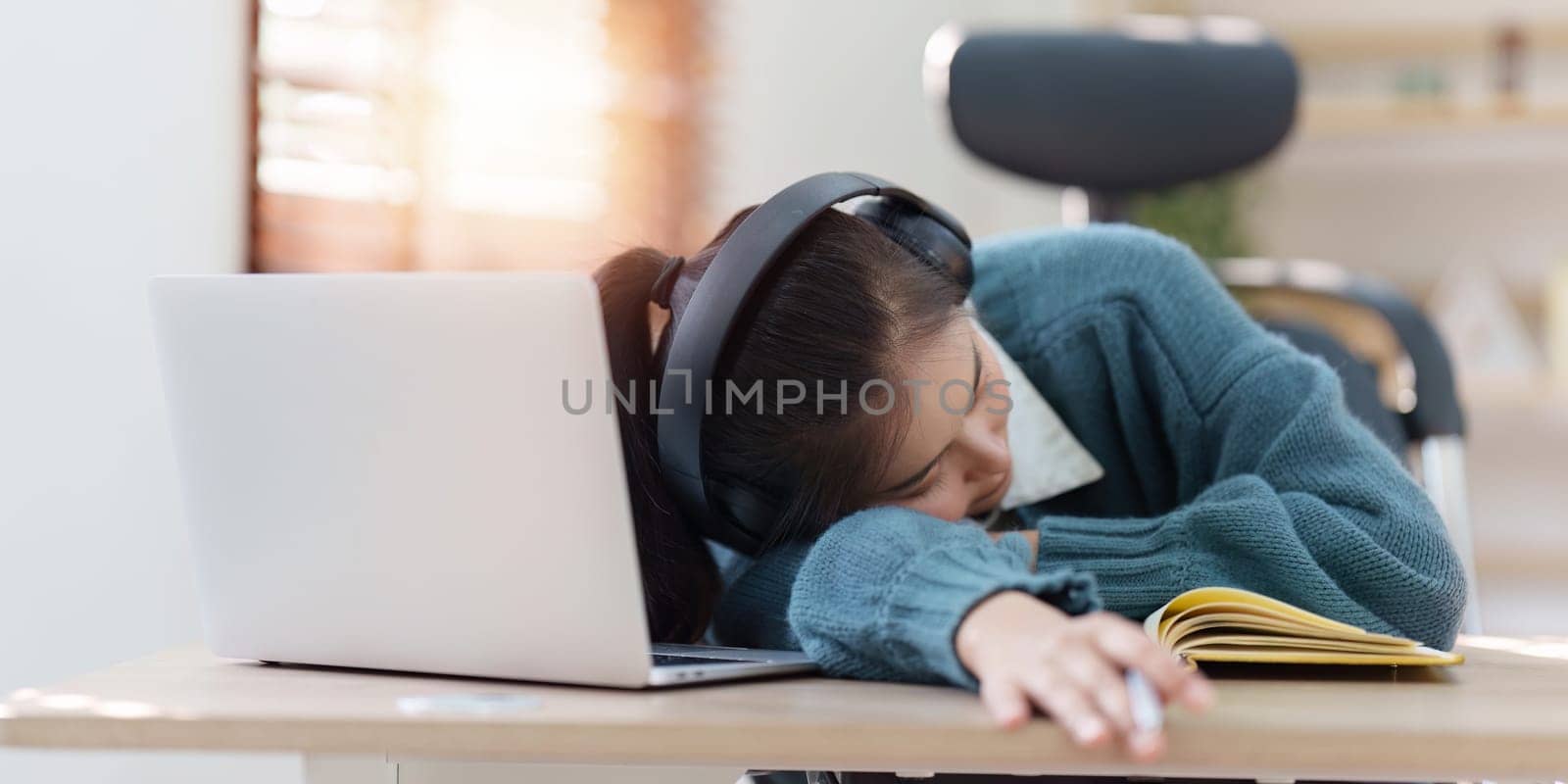 Online education, e-learning. Asian woman relaxing after studying using a laptop, listening to online lecture, taking notes, online study at home.