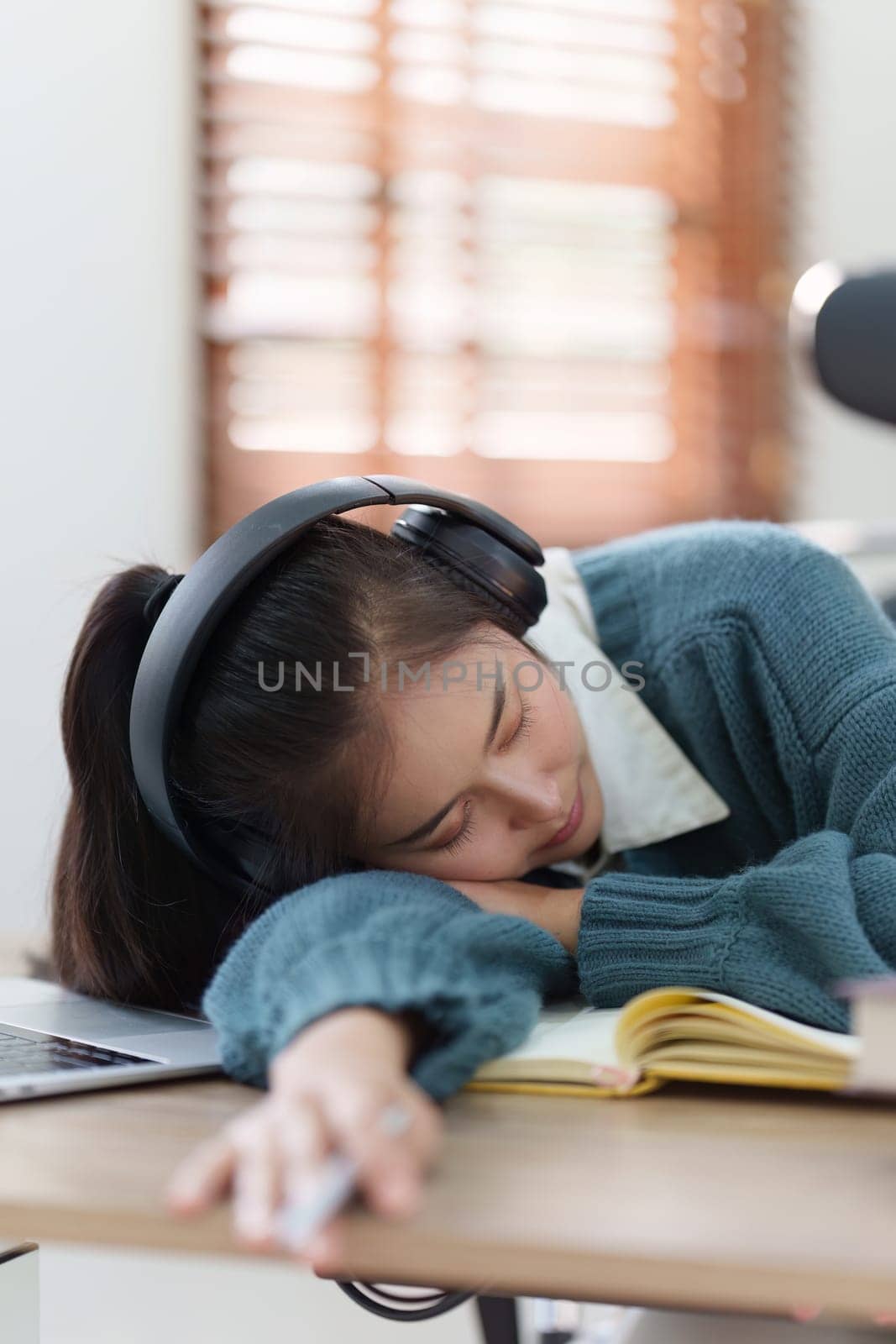 Online education, e-learning. Asian woman relaxing after studying using a laptop, listening to online lecture, taking notes, online study at home.
