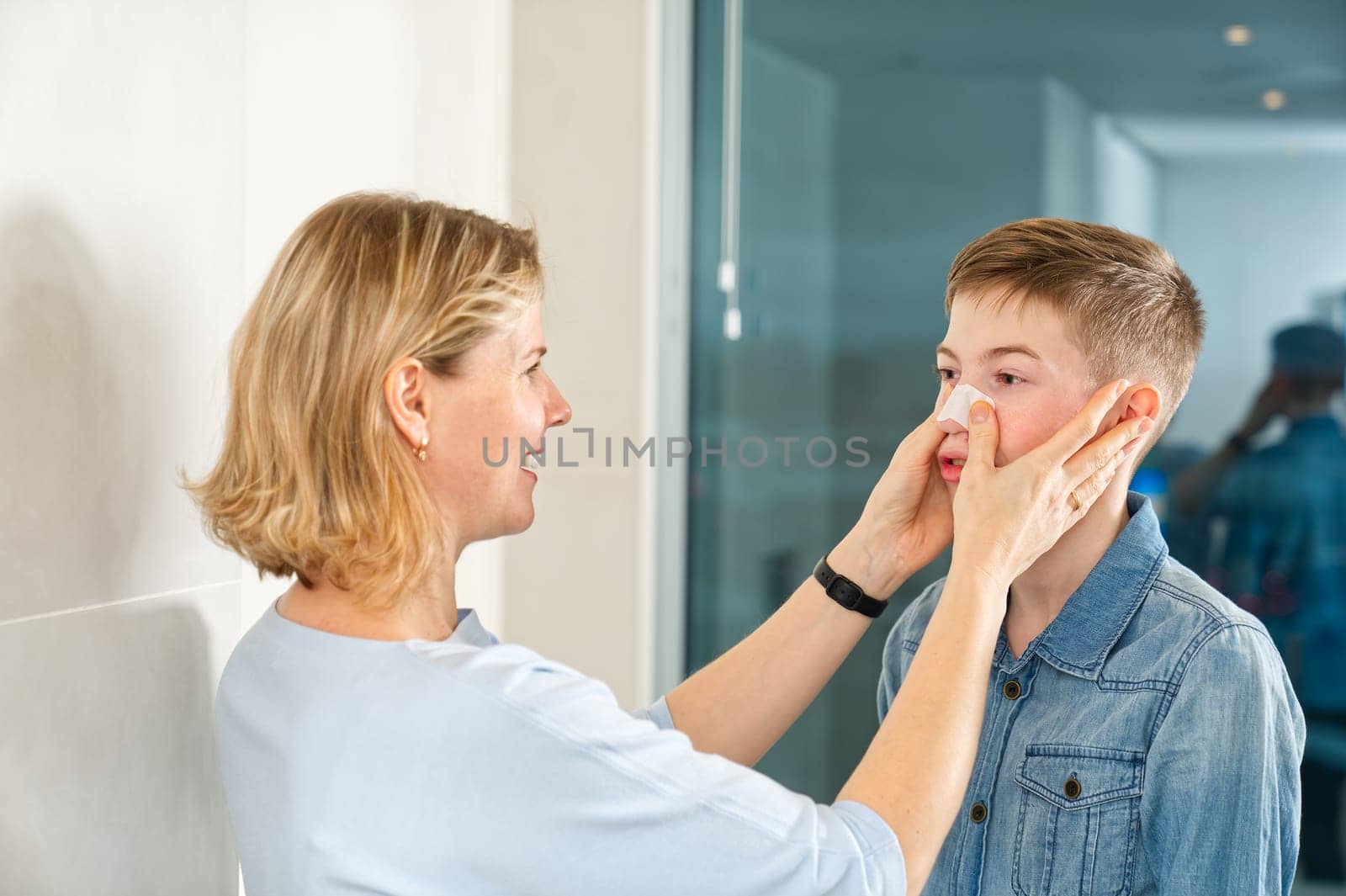 mom glues a patch to remove blackheads to her son. acne remover patch. teenage with nose band aid