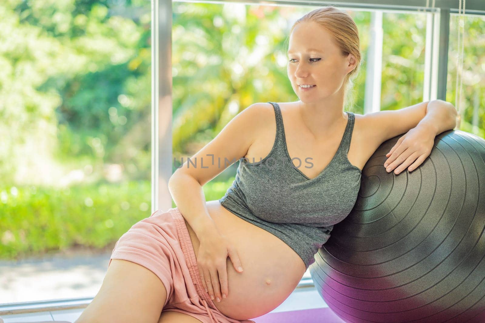 Pregnant woman exercising on fitball at home. Pregnant woman doing relax exercises with a fitness pilates ball. Against the background of the window.