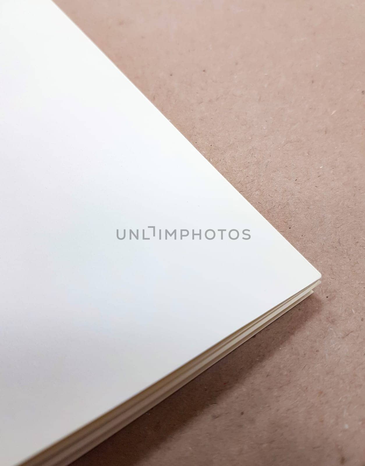 A corner of a stack of white paper sheets lies on a brown background. Space for text. Top view, vertical by claire_lucia