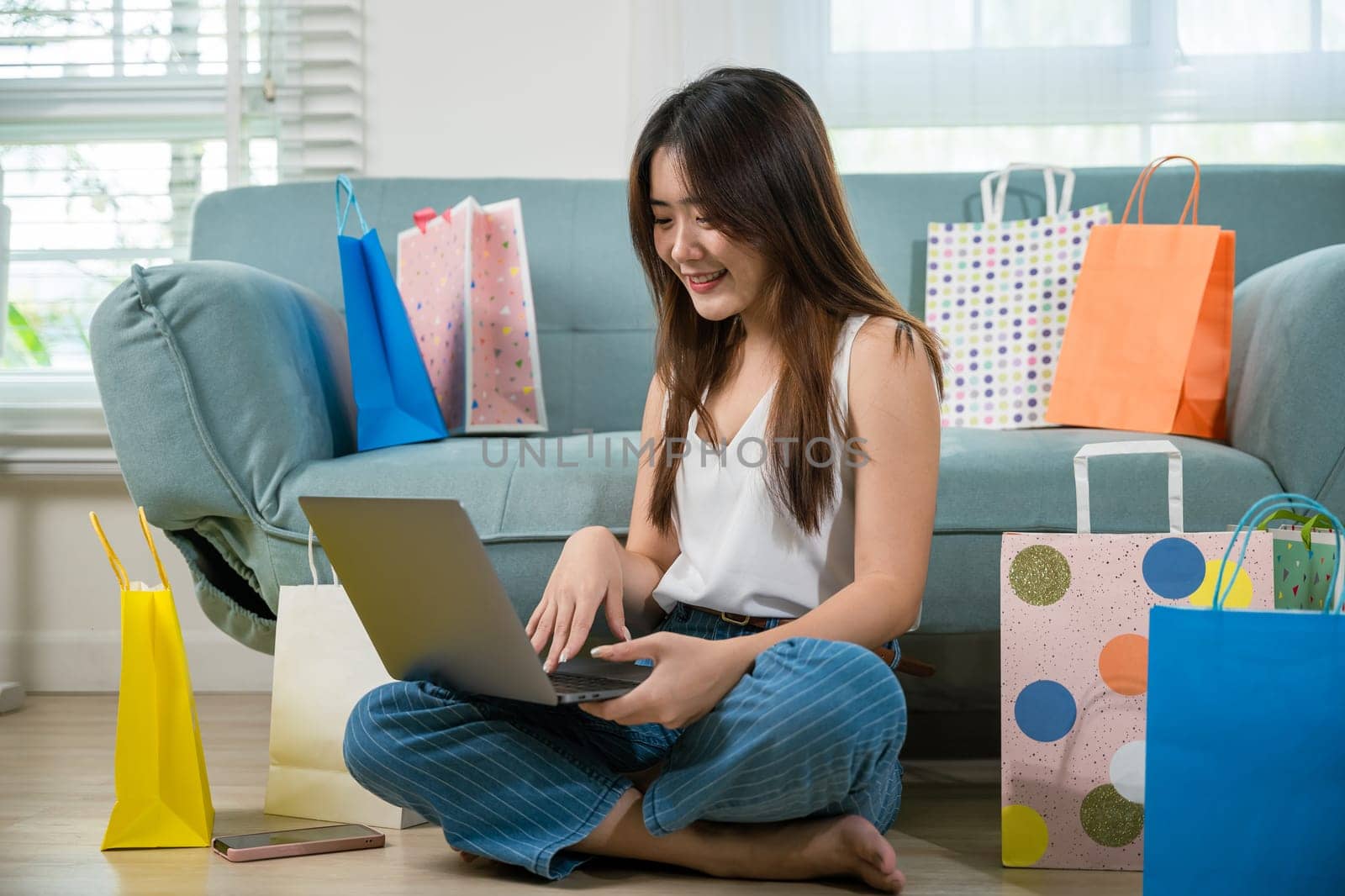 woman sitting on sofa with shopping bags using laptop computer to online shopping by Sorapop