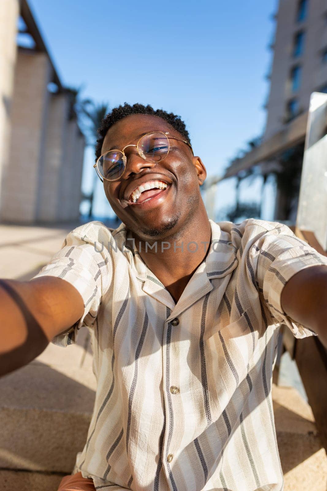 Happy young black man with glasses taking selfie looking at camera. Vertical image. by Hoverstock