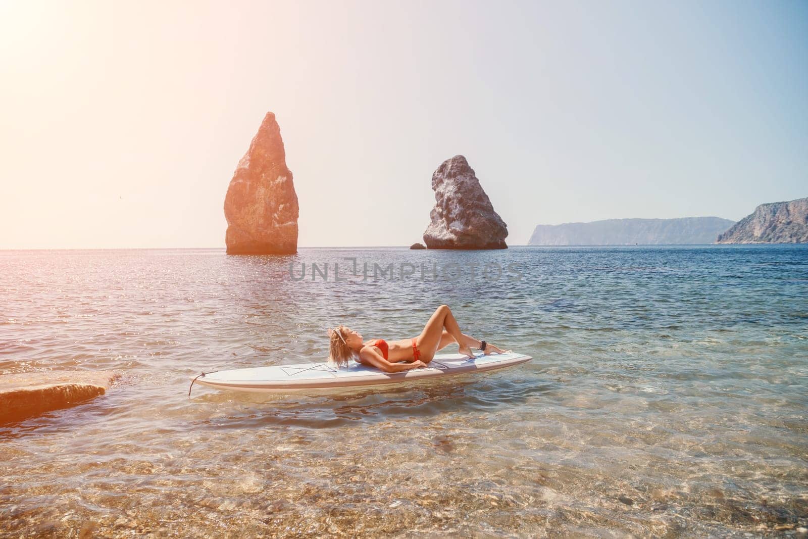 Close up shot of beautiful young caucasian woman with black hair and freckles looking at camera and smiling. Cute woman portrait in a pink bikini posing on a volcanic rock high above the sea