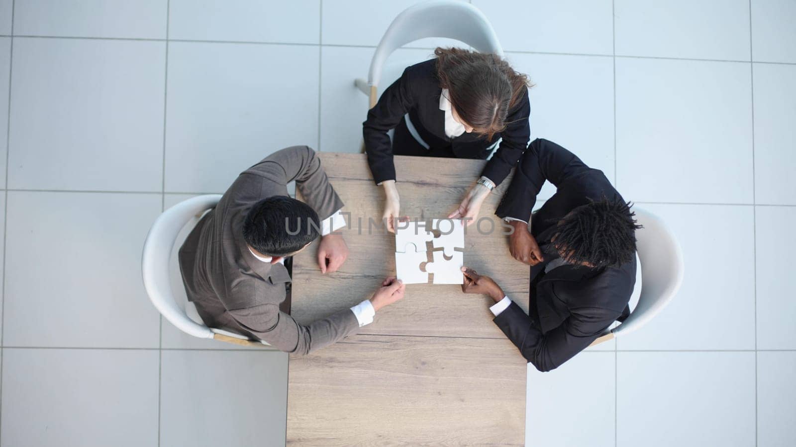 roup of business people are sitting at table and putting together puzzle top view.