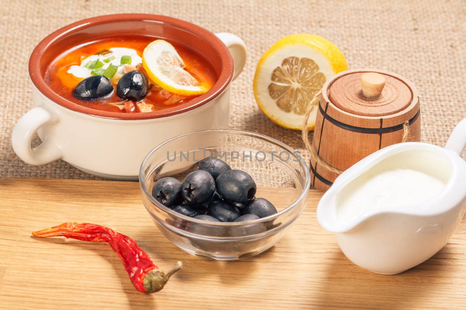 Bowl with olives, dried red pepper on cutting board and ceramic soup bowl with saltwort, sauceboat and cut lemon. by mvg6894