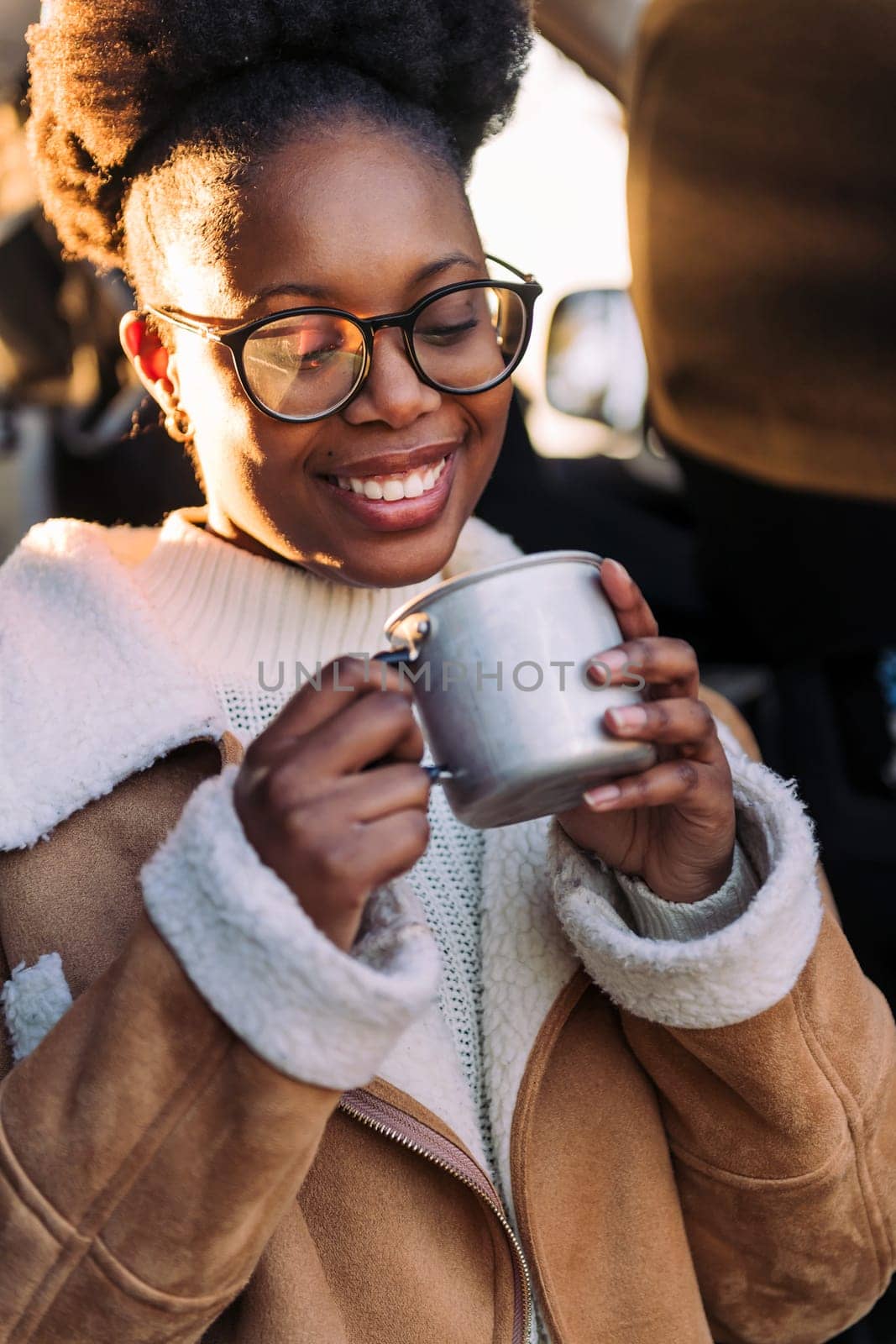 young black woman smiling happy sitting in a camper van drinking a cup of coffee at sunset, concept of van life and weekend getaway