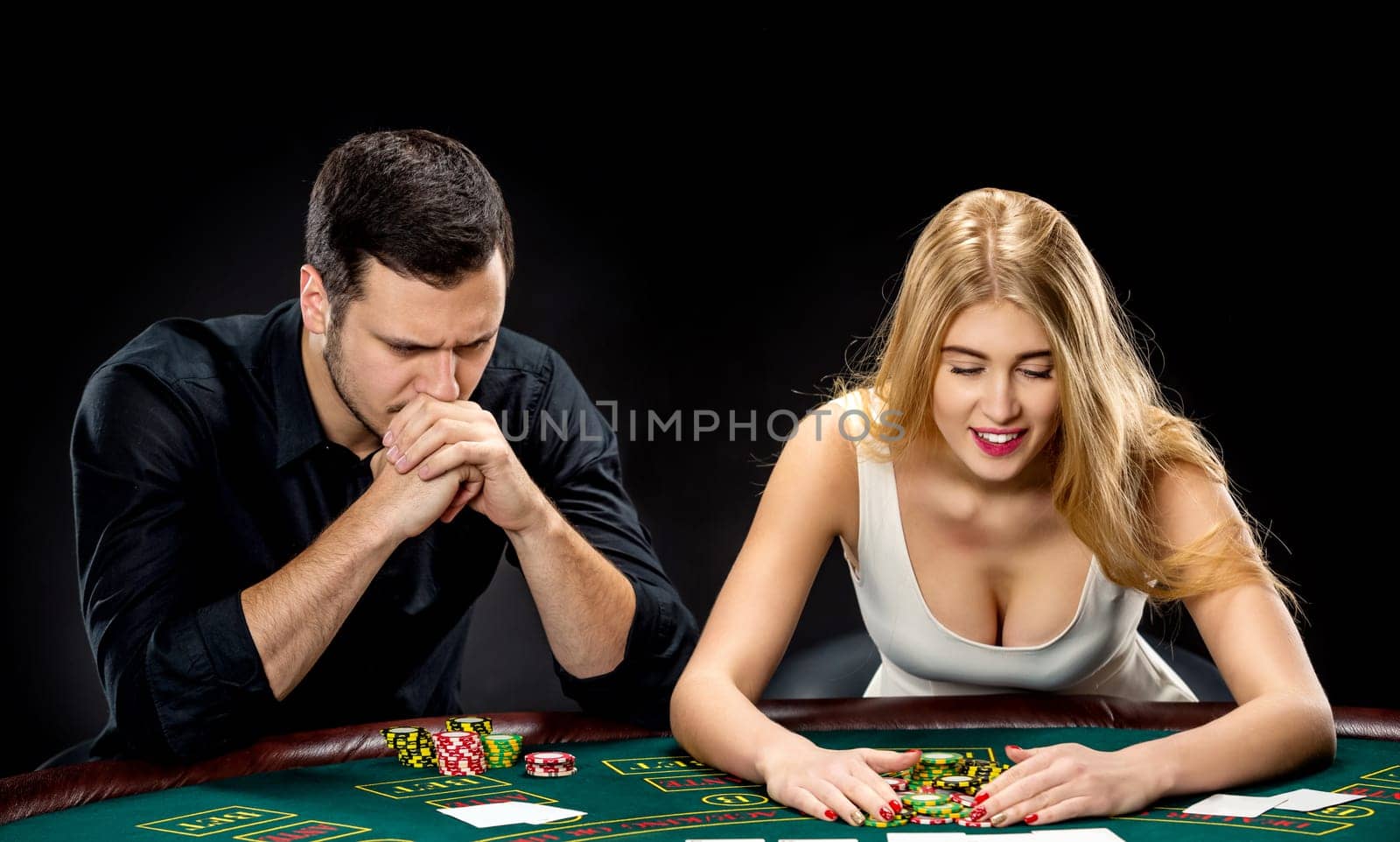 Two poker players sitting at a poker table on black background and going all-in pushing his chips forward