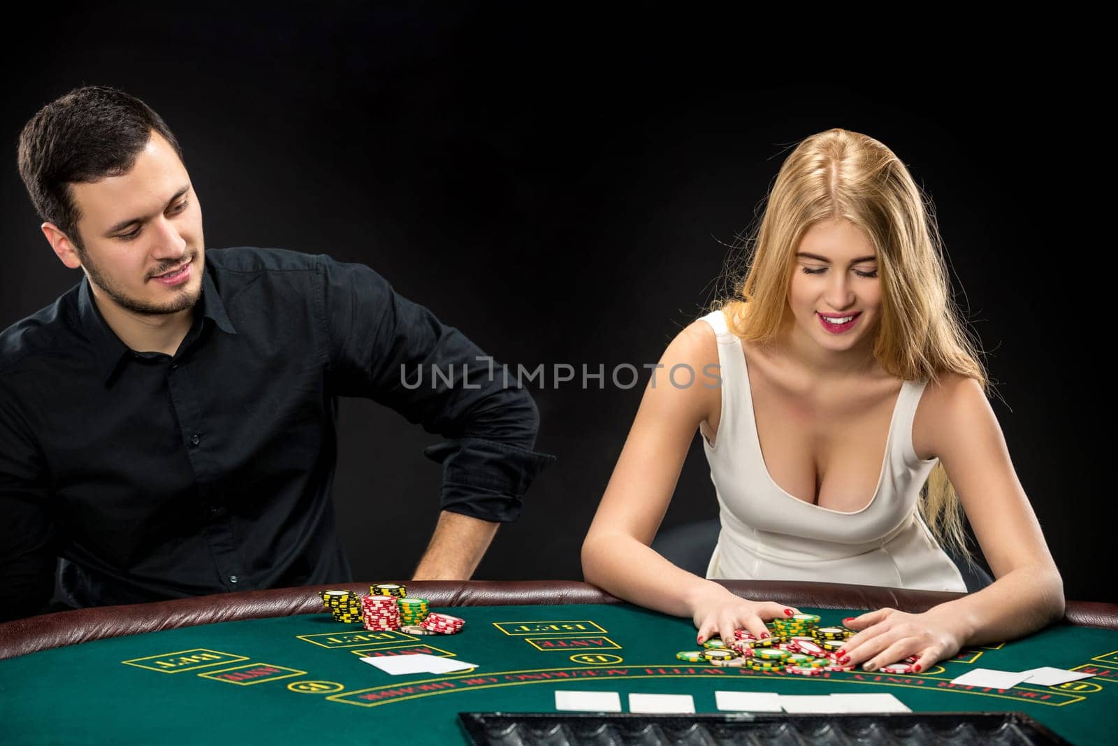 Young couple playing poker and have a good time in casino, woman taking poker chips after winning