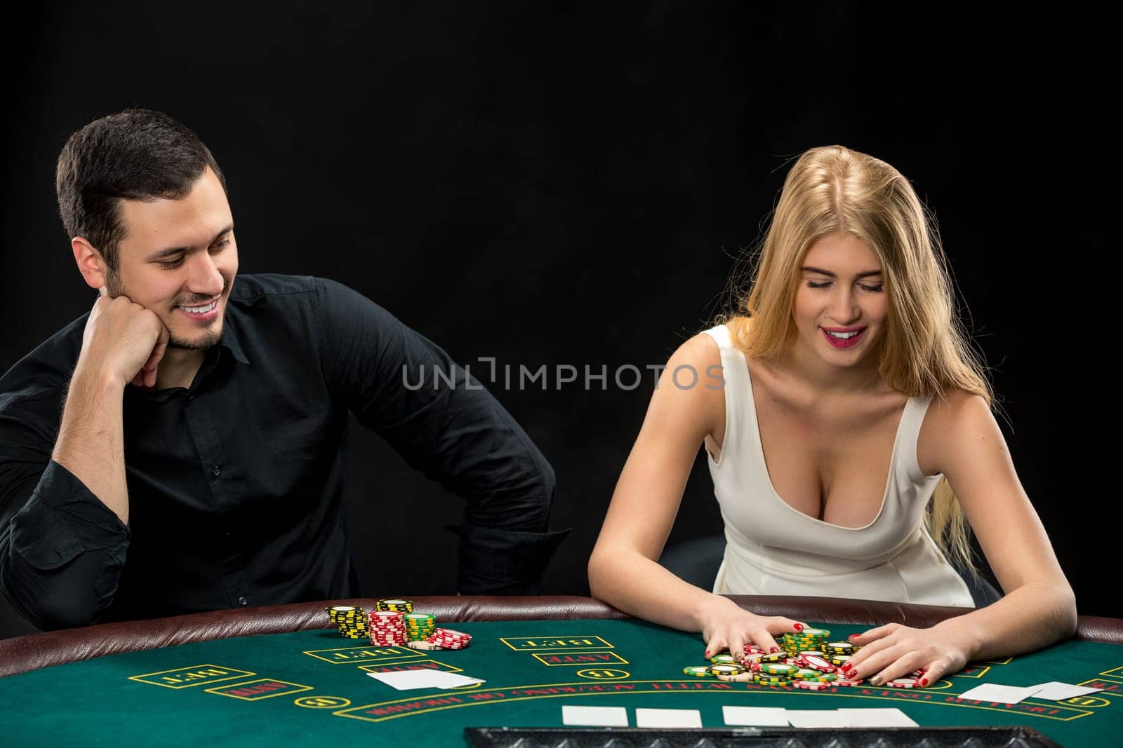 Young couple playing poker and have a good time in casino, woman taking poker chips after winning