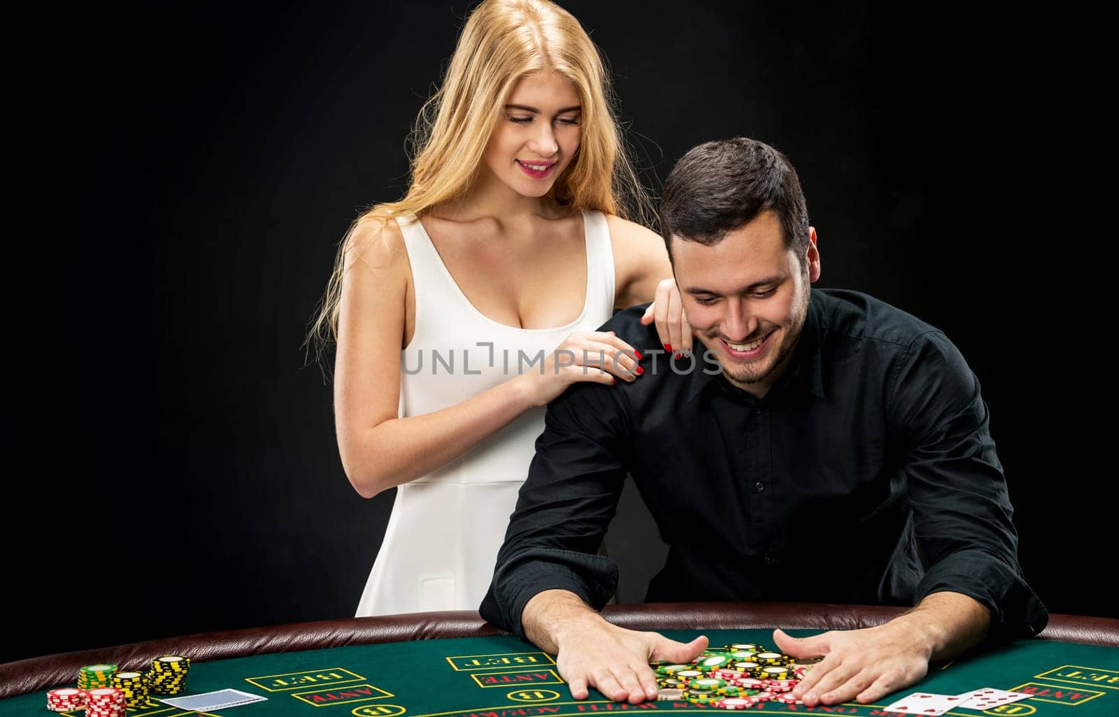 Young couple playing poker and have a good time in casino. Man taking poker chips after winning, woman embracing his