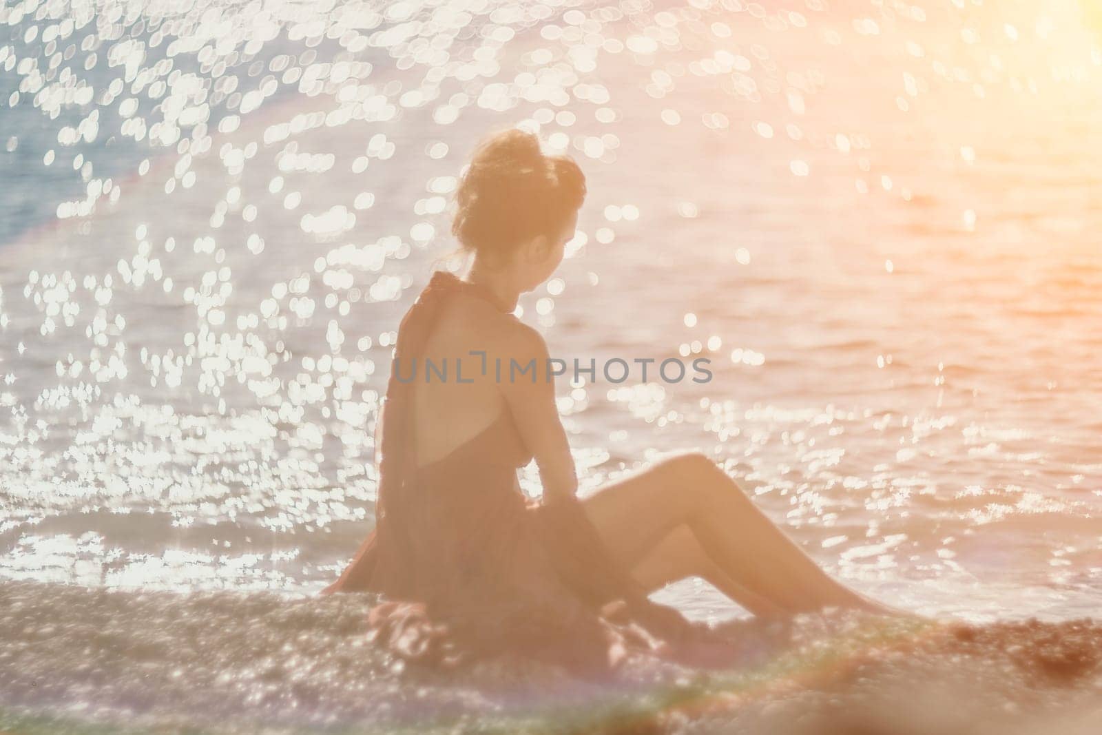 Woman in red dress on sea. Side view a Young beautiful sensual woman in a red long dress posing on the beach near sea on sunset. Girl on the nature on blue sky background. Fashion photo. by panophotograph