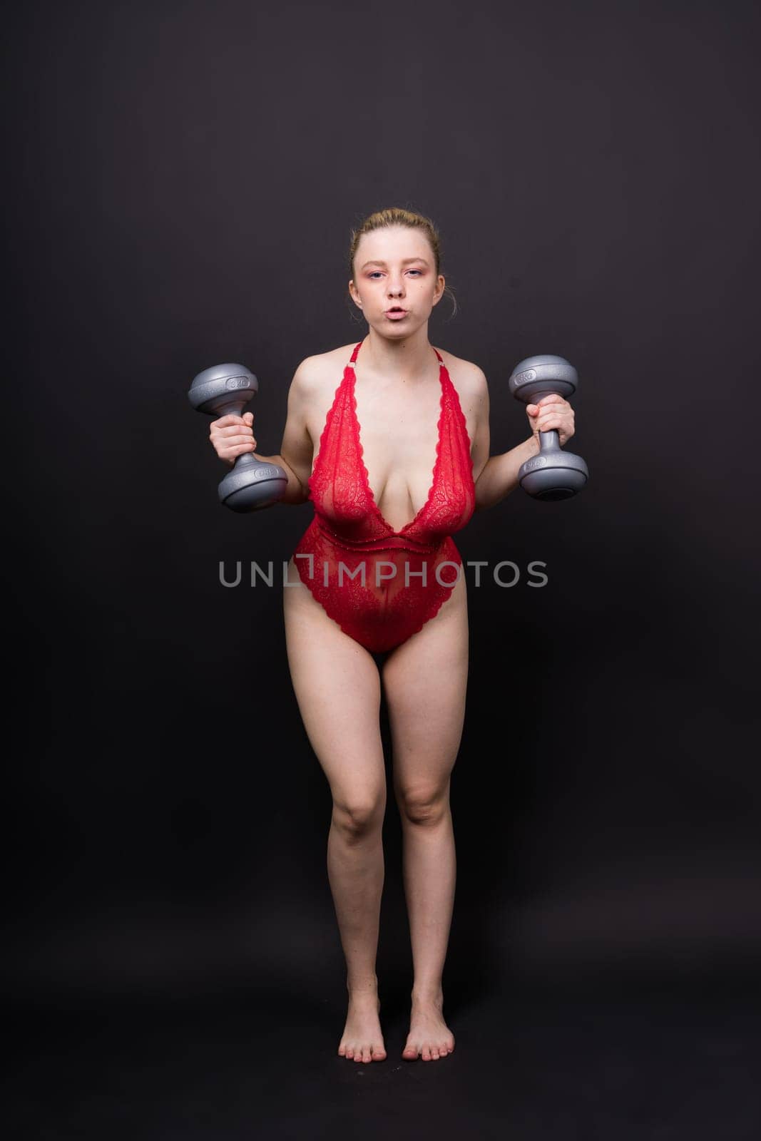 Beautiful model in sportswear with dumbbells looks at camera on yellow, red and dark background