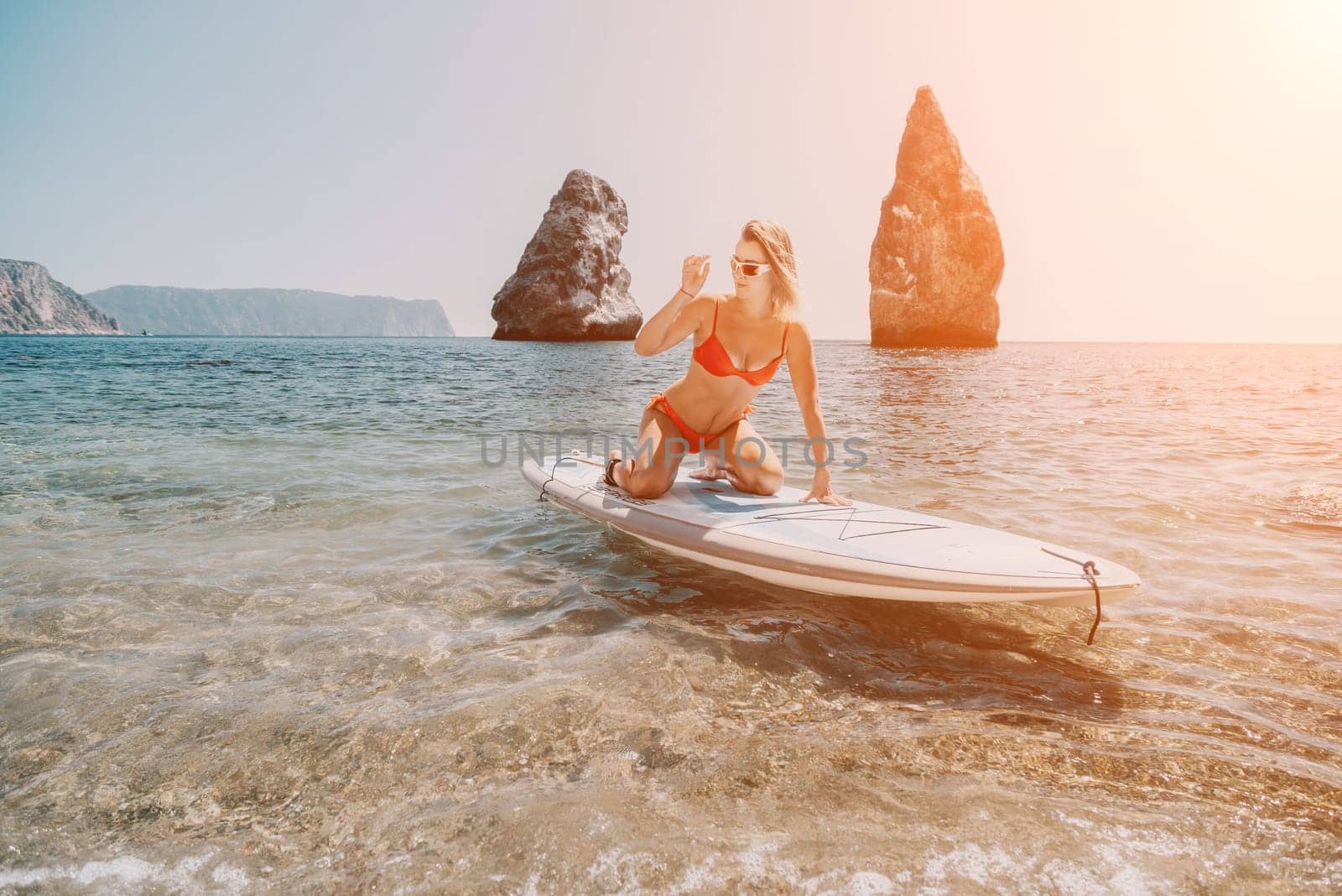 Woman sea sup. Close up portrait of happy young caucasian woman with blond hair looking at camera and smiling. Cute woman portrait in red bikini posing on sup board in the sea by panophotograph