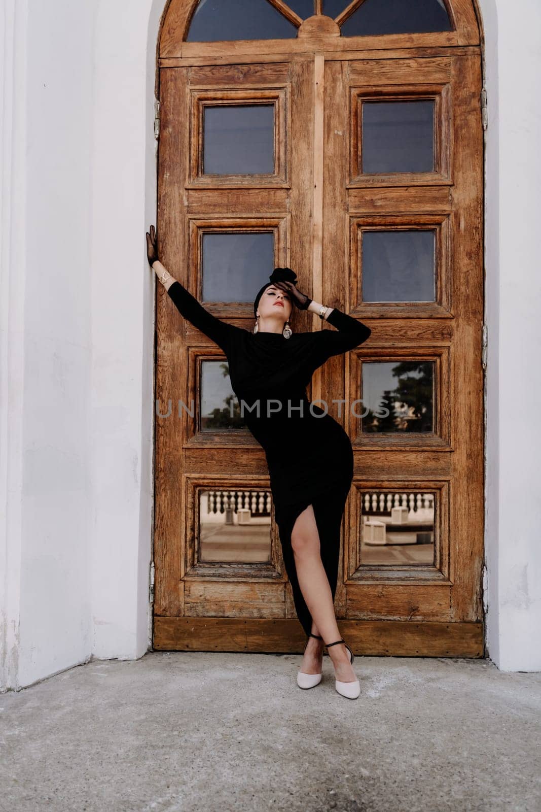 Stylish woman in the city. Fashion photo of a beautiful model in an elegant black dress posing against the backdrop of a building on a city street.