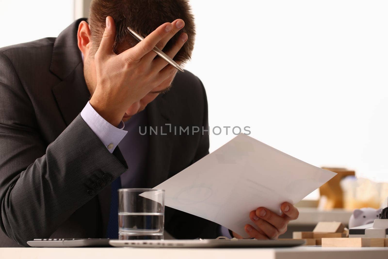 Stressed businessman with headache or migraine working at office desk. Bankruptcy depression and loan documents with debts