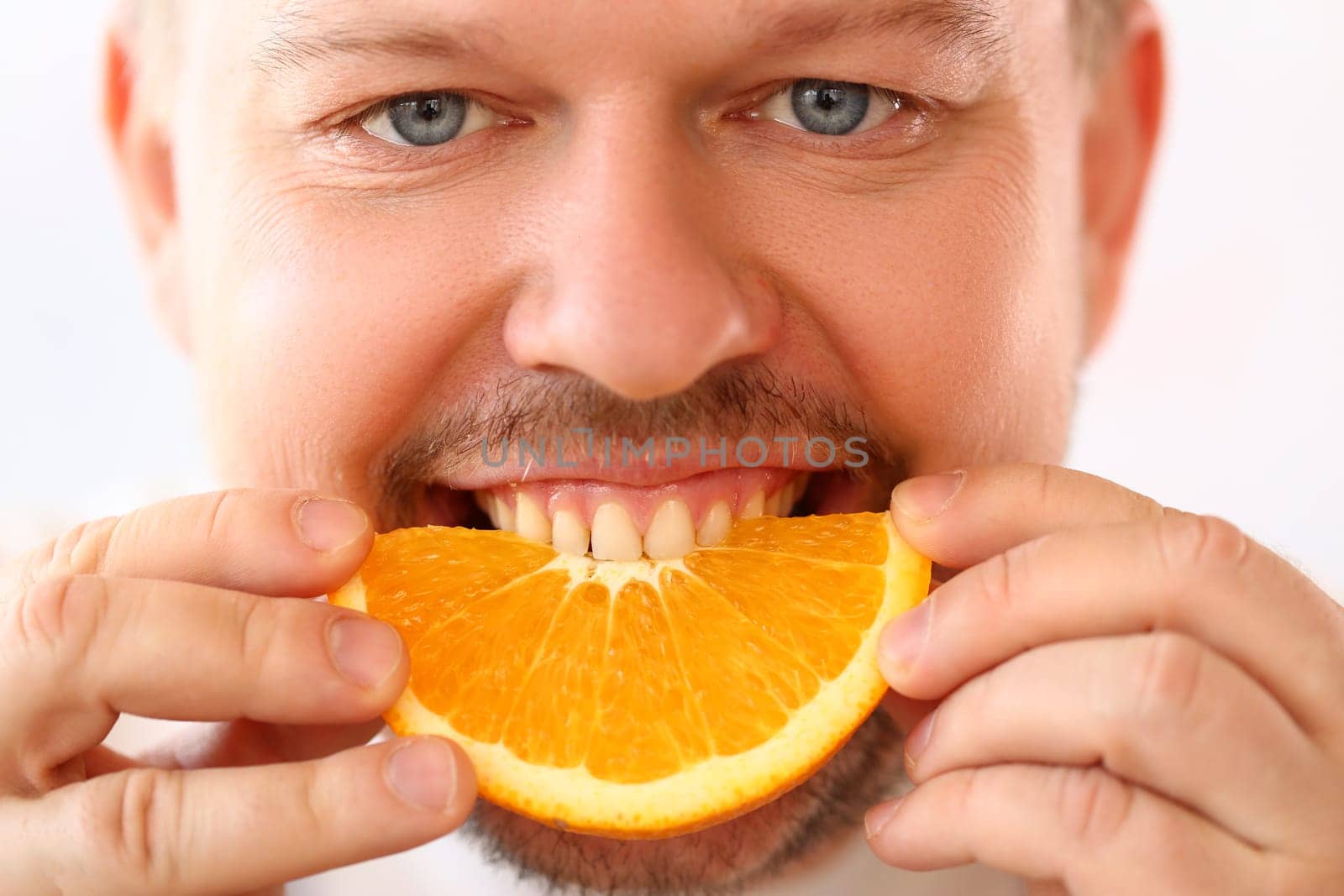 Portrait of smiling man with slice of juicy orange. Vitamins antioxidants in citrus fruits