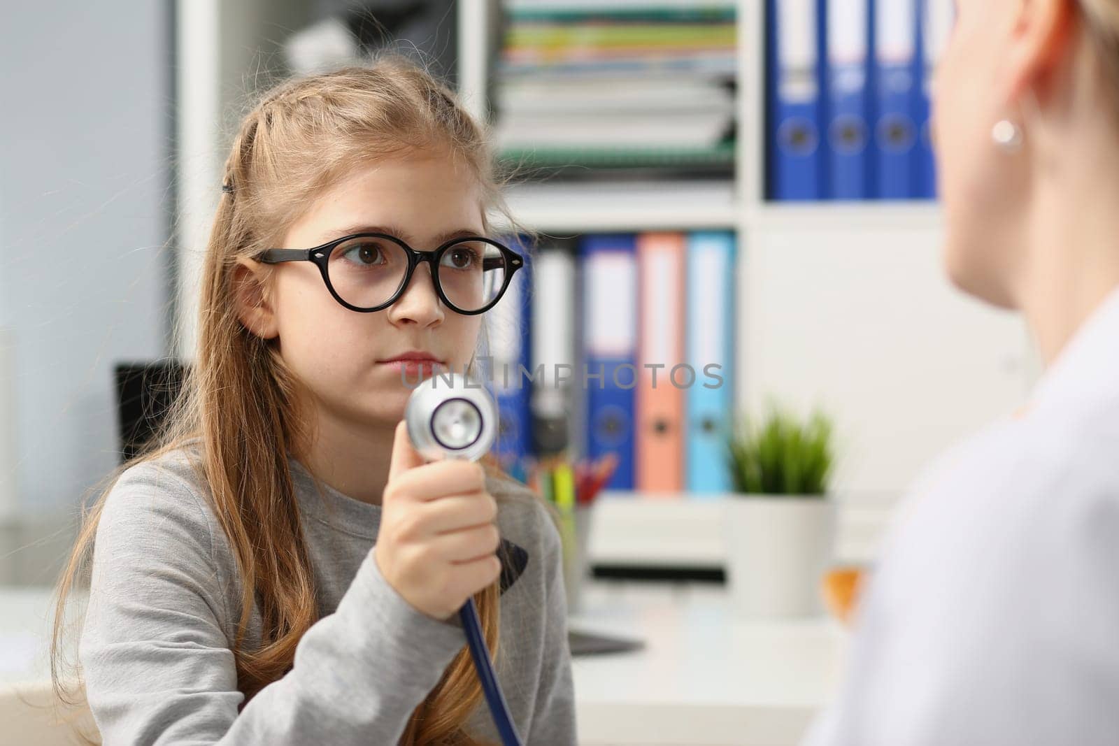 Girl child on medical examination holds stethoscope. Smiling child trusts doctor pediatrist