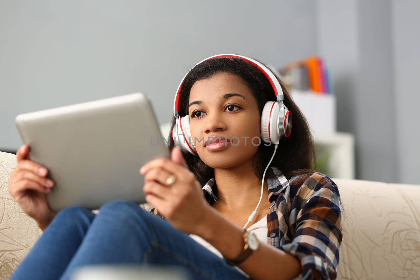 Focused black woman studying foreign language online. Remote female student in virtual classroom sitting on sofa in headset and holding tablet