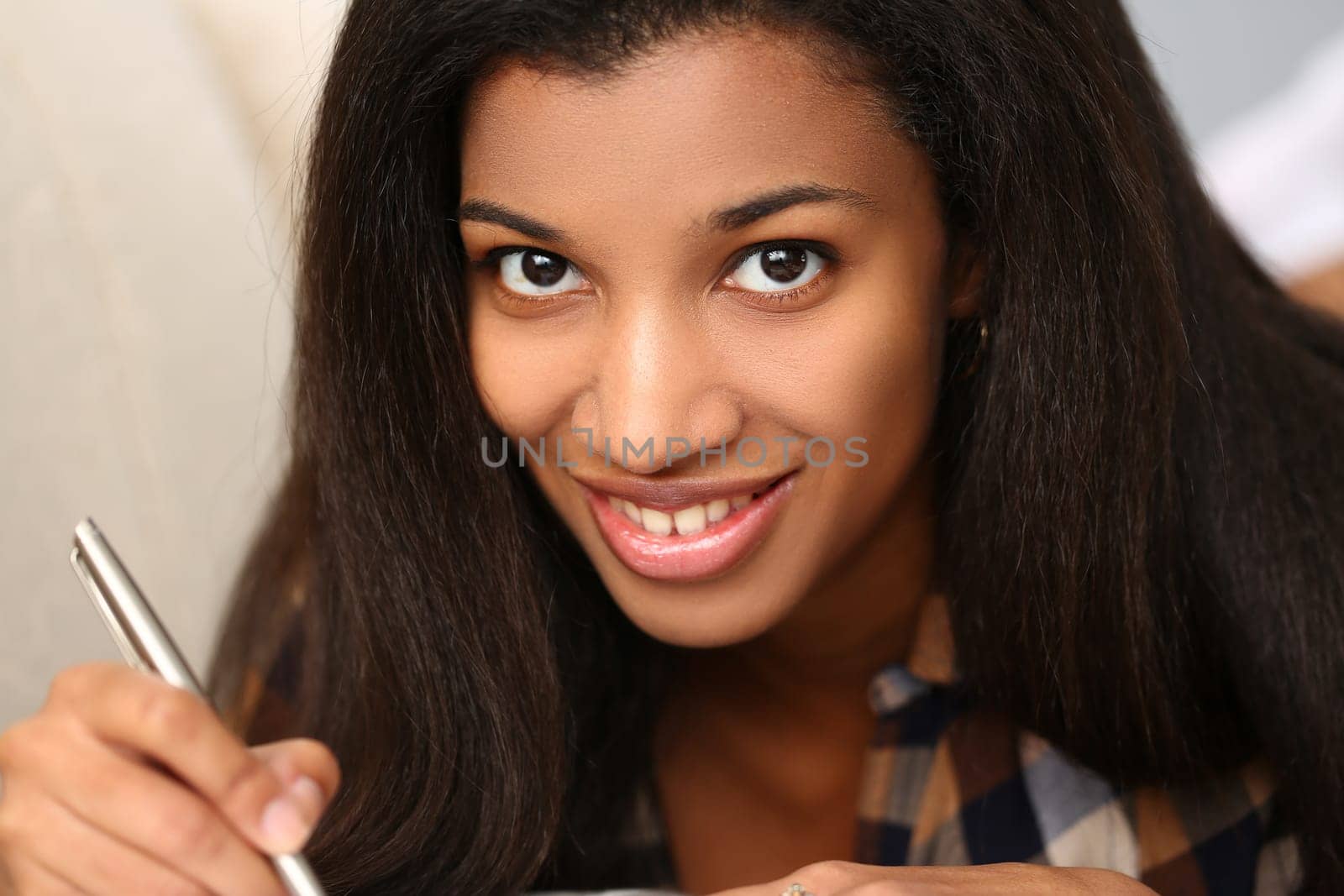 Young black woman writes in a magazine while lying on couch. Portrait of beautiful smiling woman with pen