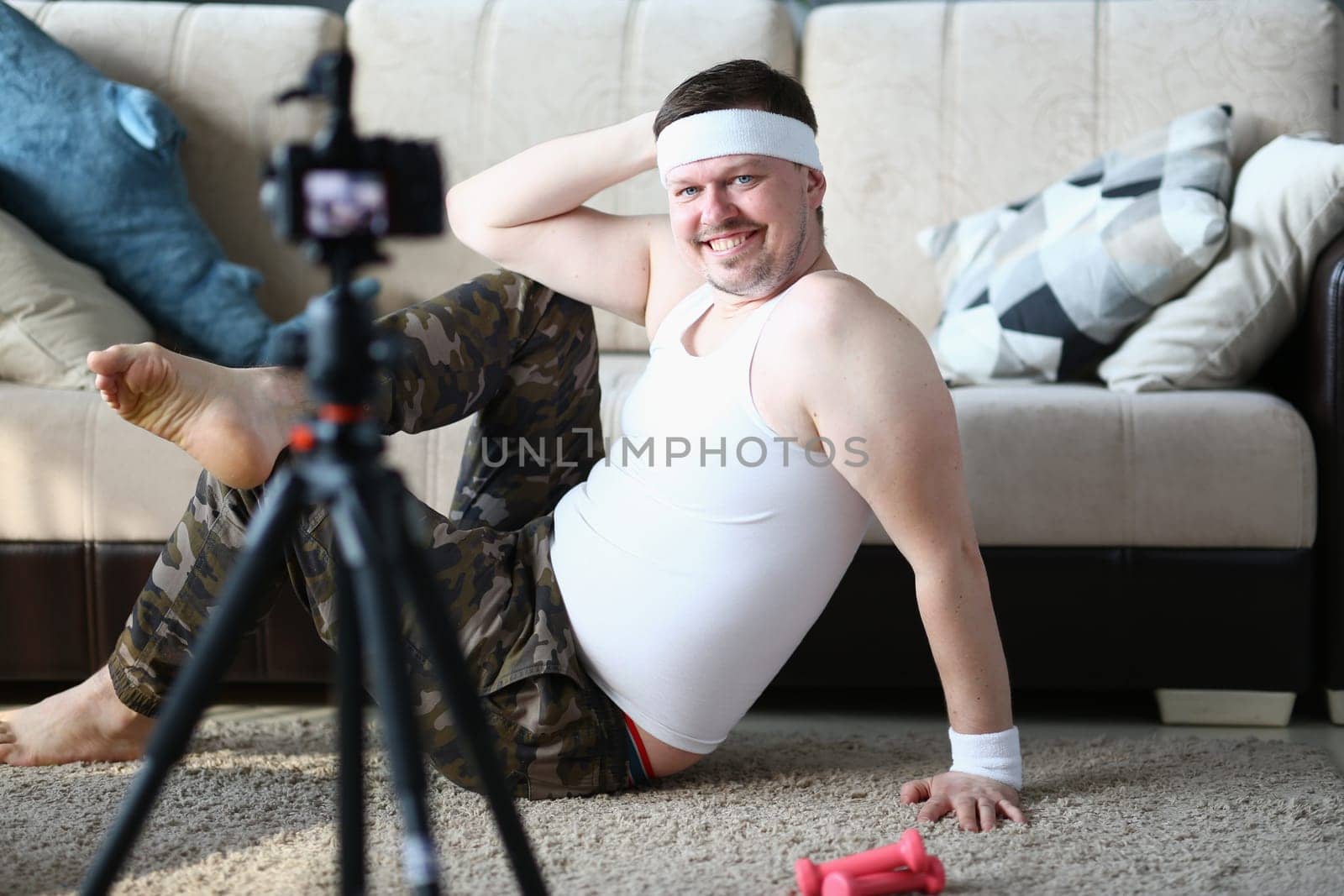 Athletic fat smiling man is recording workout on camera. Positive and helpful fitness blog for health and diet