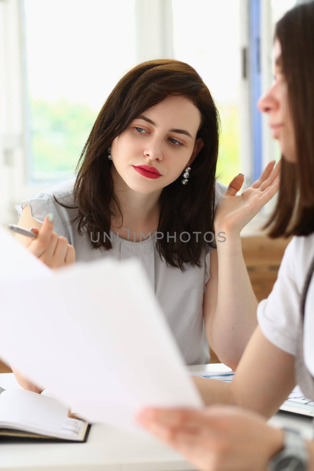 Two business women are discussing a financial report holding documents with graphs and charts in their hands by kuprevich