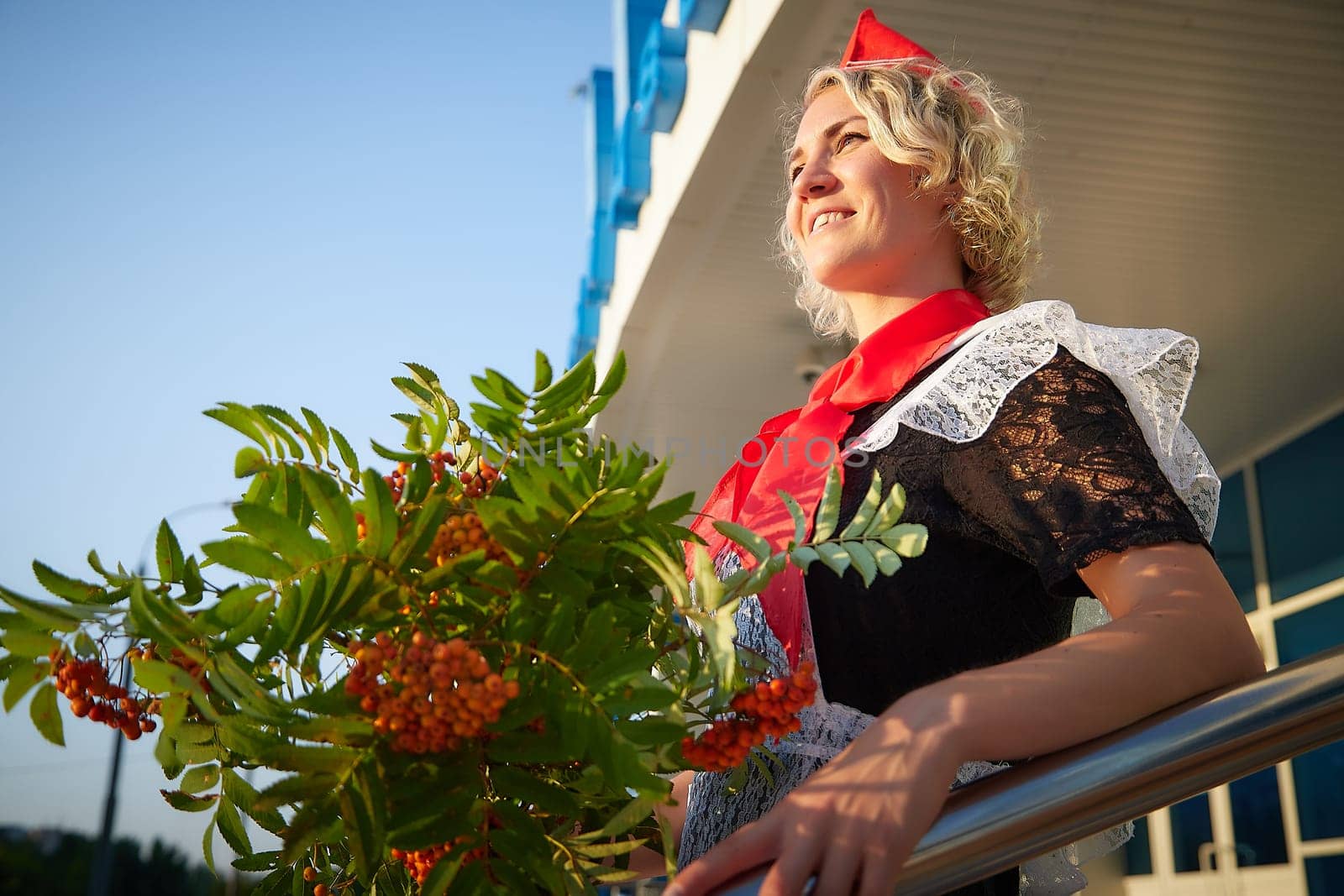 A Girl in black school uniform, white apron and red tie on steps of school with bouquet of flowers. Nostalgia photo shoot of teenager of female pioneer from USSR costume for September 1 or graduation