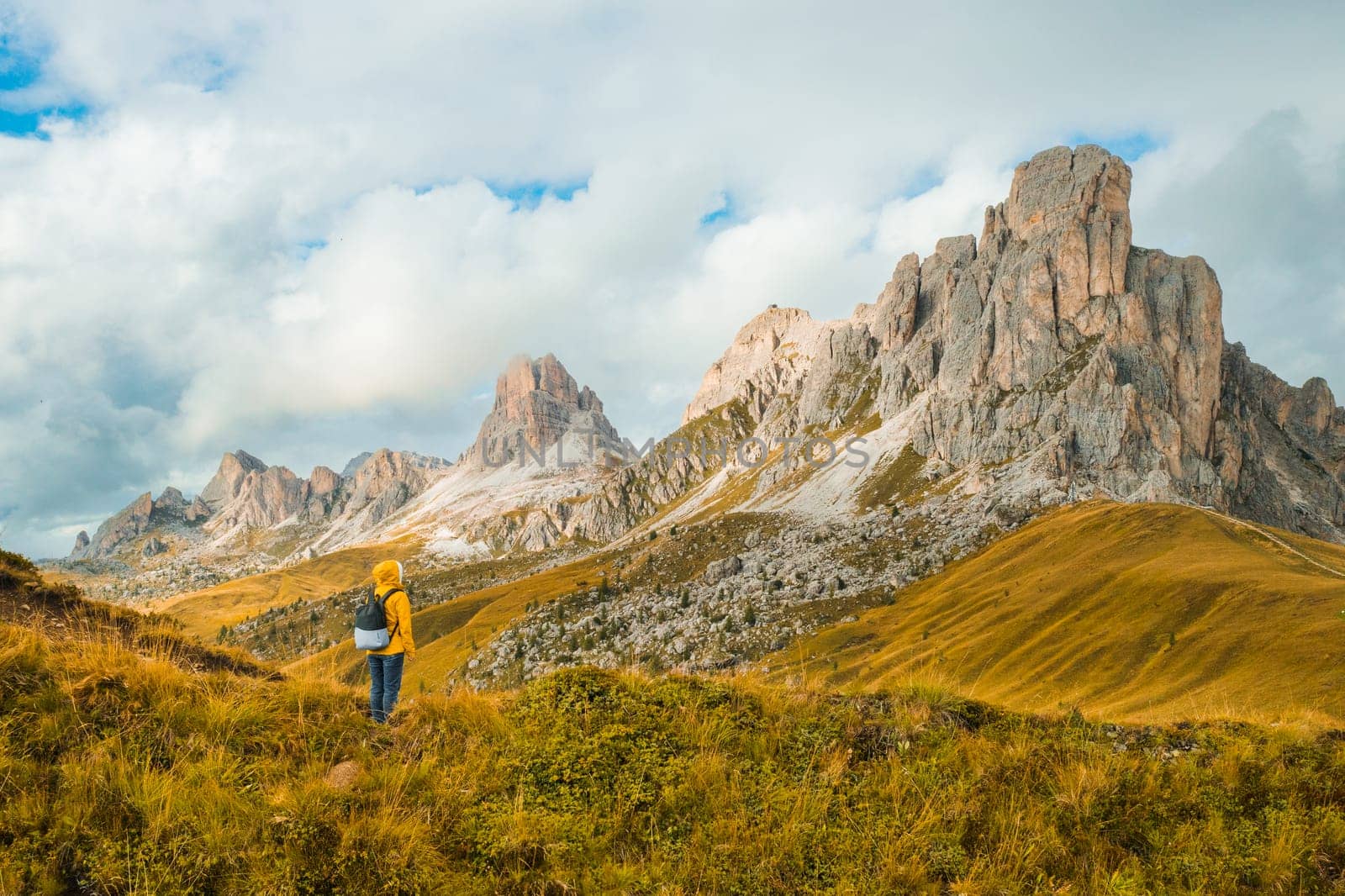 Tourist in yellow jacket and backpack enjoying the exploration amidst the towering mountains of the famous Giau Pass.