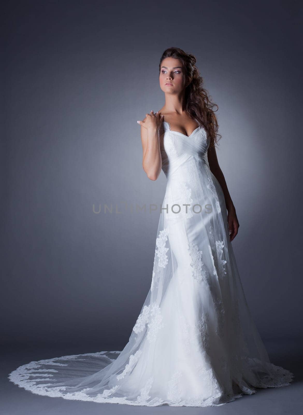 Beautiful slim bride posing in elegant long dress, on gray background