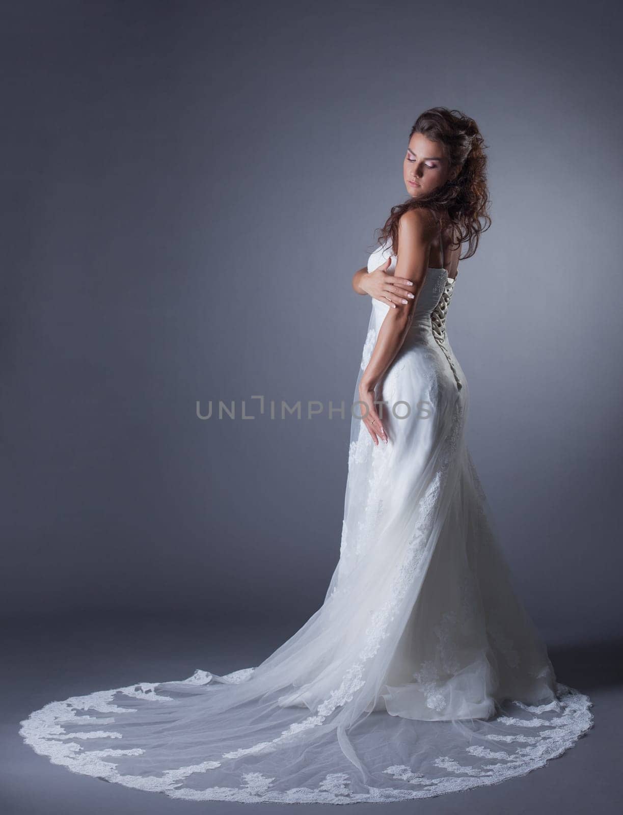 Slender brunette posing in stylish wedding dress, on gray background