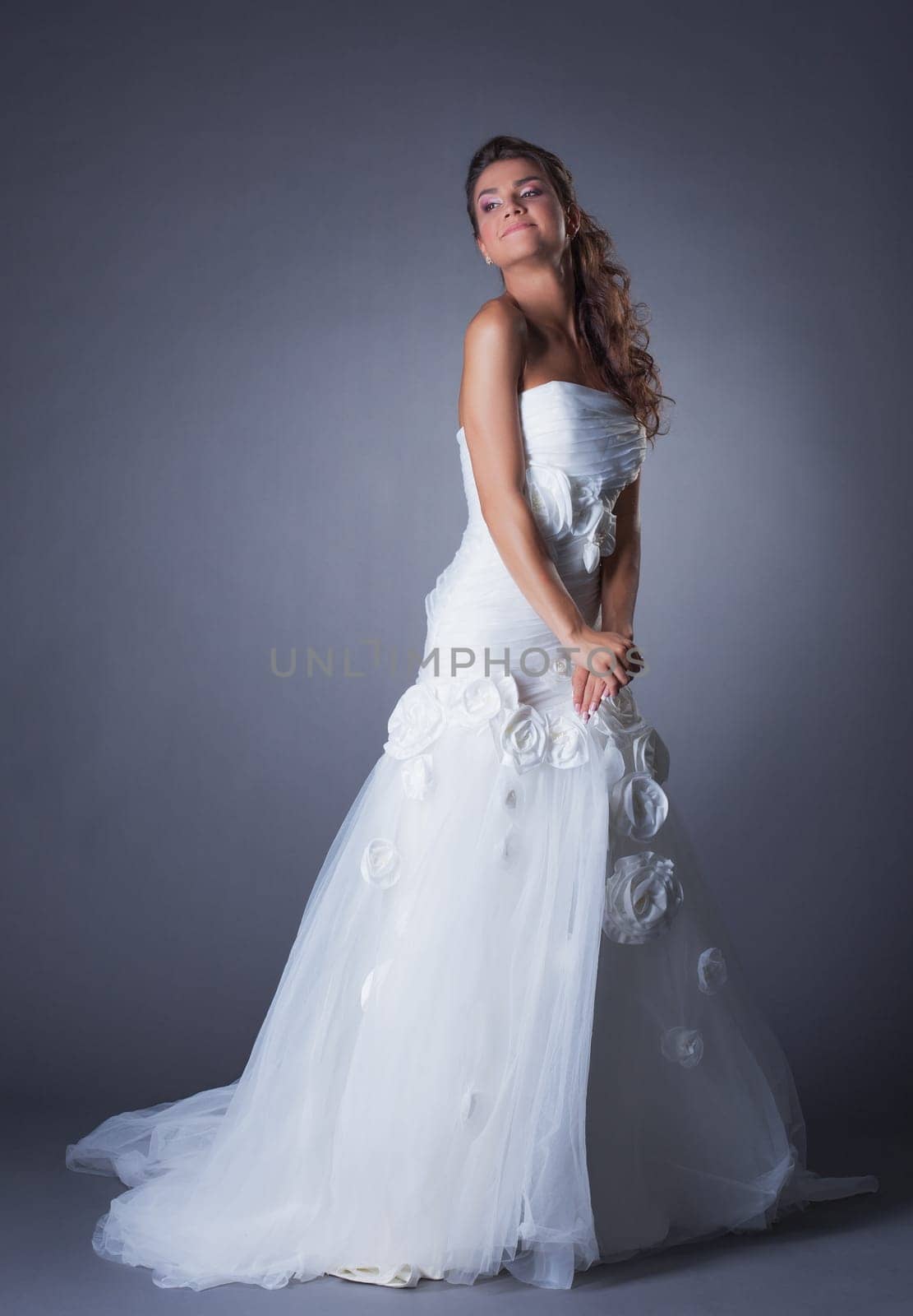 Dreamy brunette posing in elegant wedding dress, on gray background