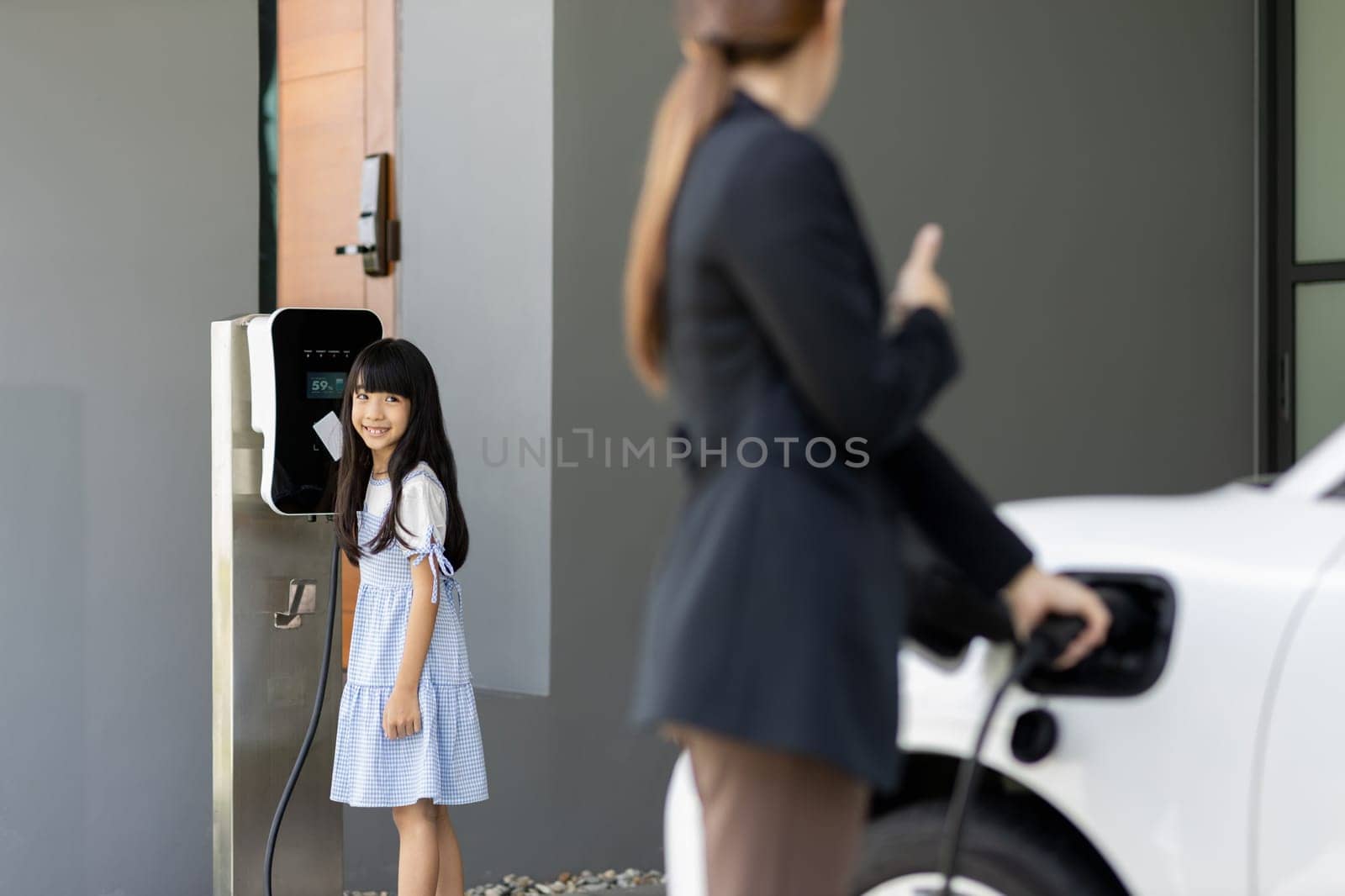 Progressive lifestyle of mother and daughter who have just returned from school in an electric vehicle that is being charged at home. Electric vehicle powered by sustainable clean energy.