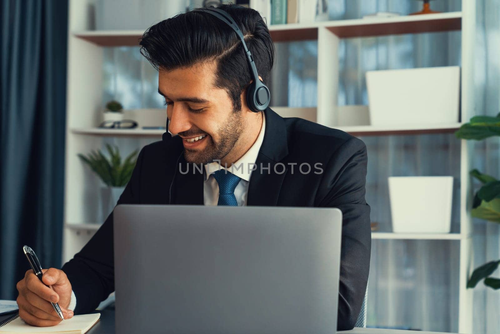 Male call center operator or telesales representative siting at his office desk wearing headset and engaged in conversation with client providing customer service support or making a sale. fervent