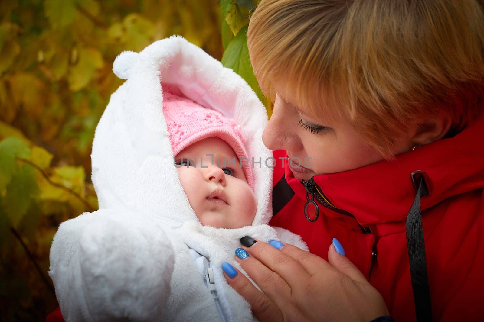 Kirov, Russia - October 23, 2022: Adult grandmother with a baby grandson or granddaughter in nature among the greenery. A woman with small child in the park in autumn, summer, spring