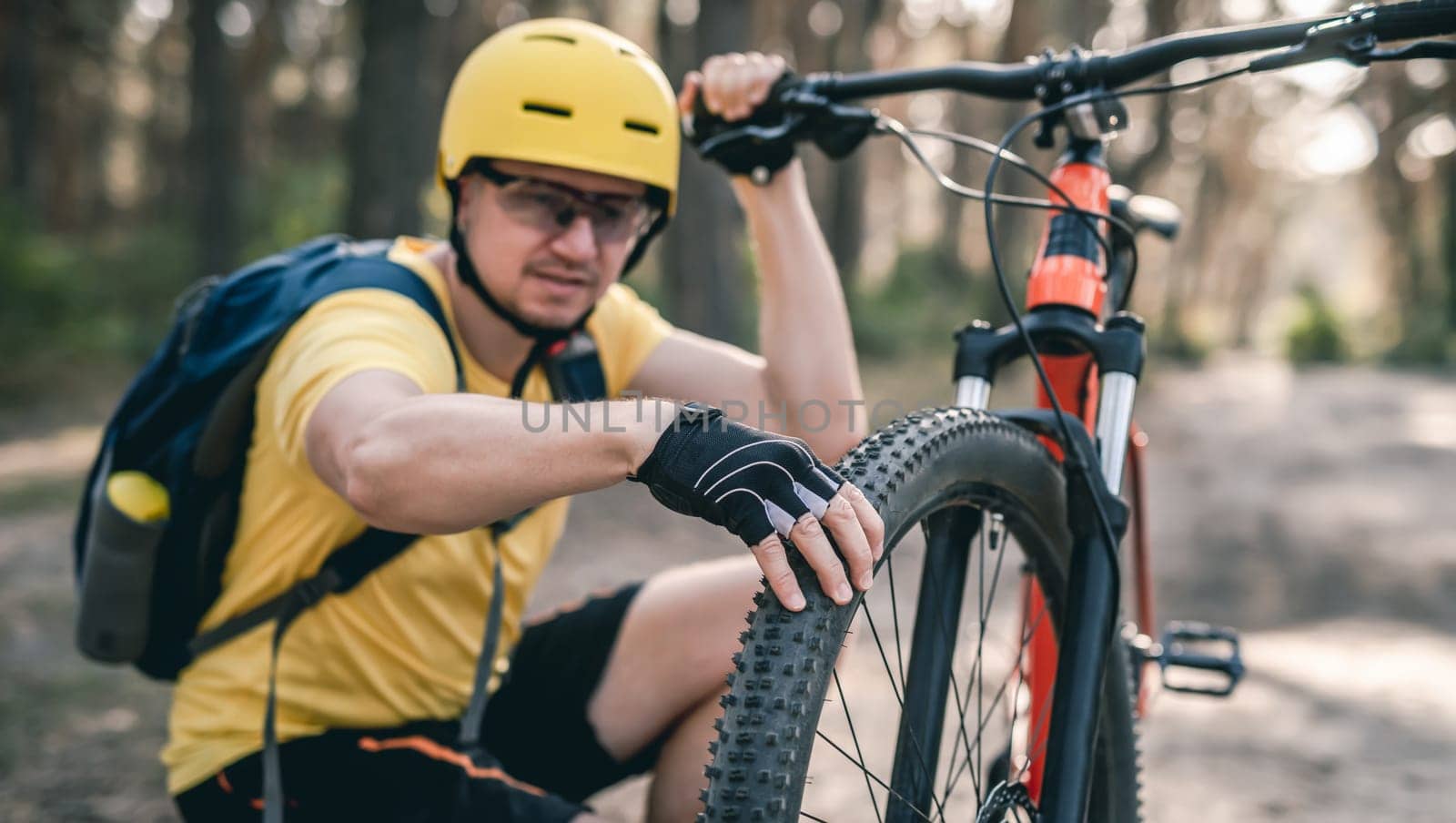 Man cyclist checking bicycle tire pressure before ride in forest