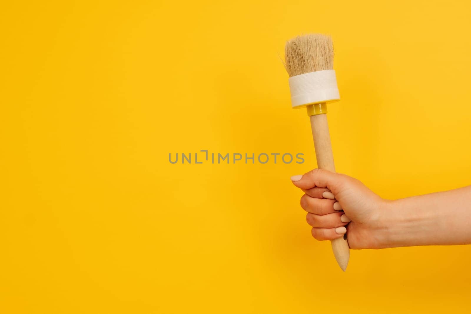 Woman hand holding wooden paint brush up on yellow background with copy space. Concept of creativity and inspiration. Working tool for home design project